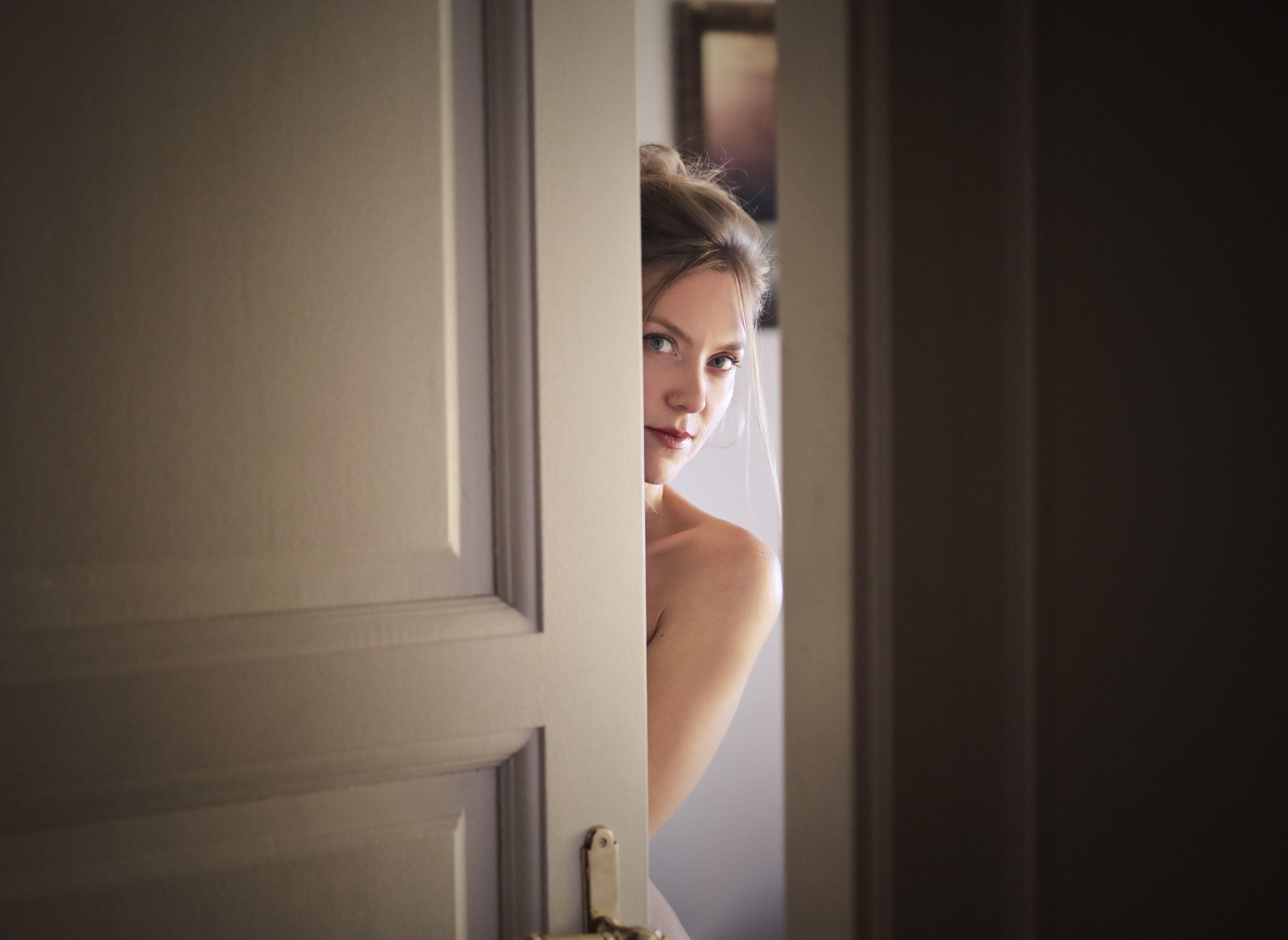 A woman peeks through a slightly opened door, creating a mysterious and intriguing atmosphere.