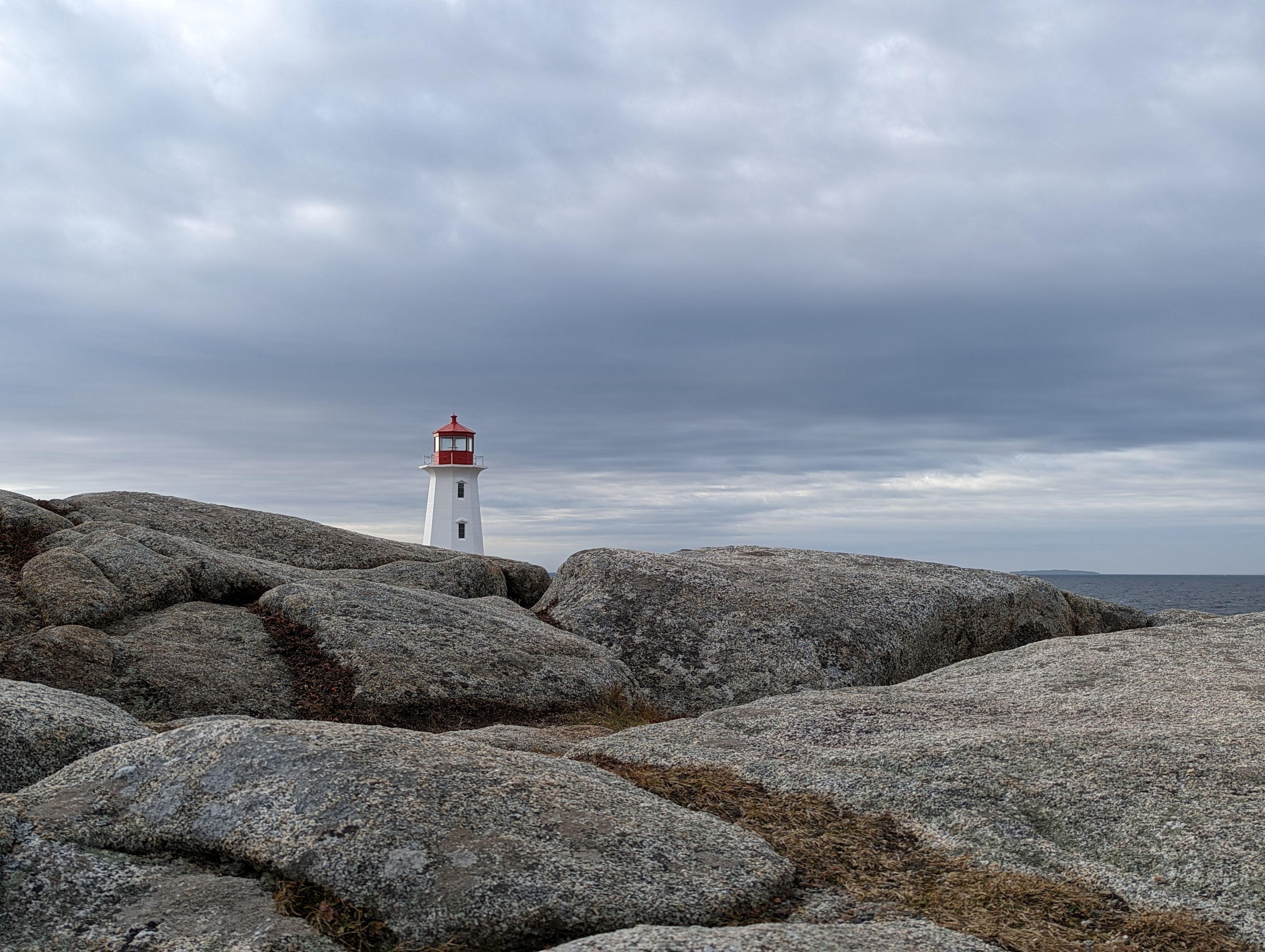 Iconic lighthouse at Peggy's Cove, Nova Scotia, stands amidst rugged rocks under a cloudy sky.