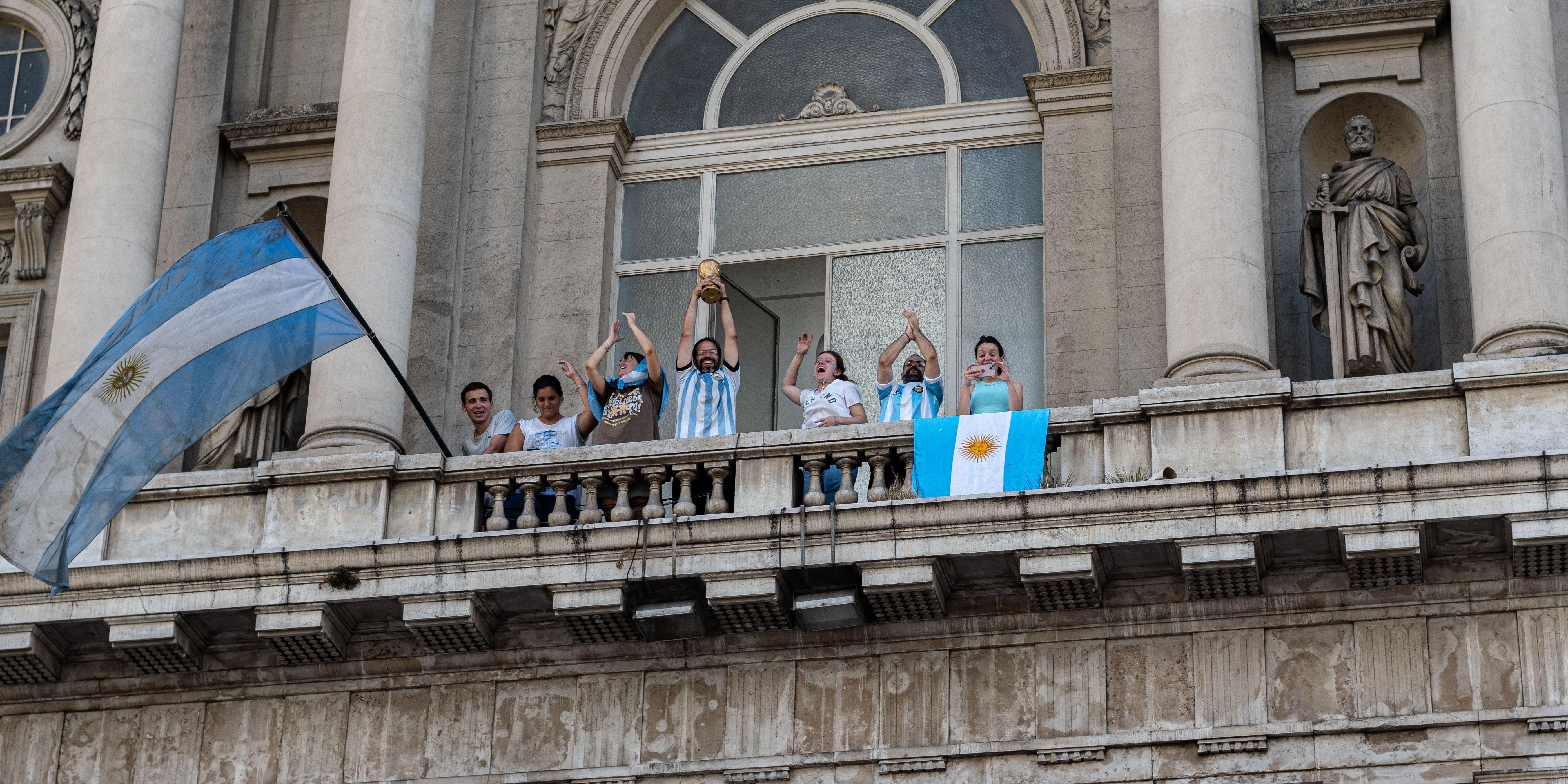 People celebrating with flags and a trophy on a Buenos Aires balcony.