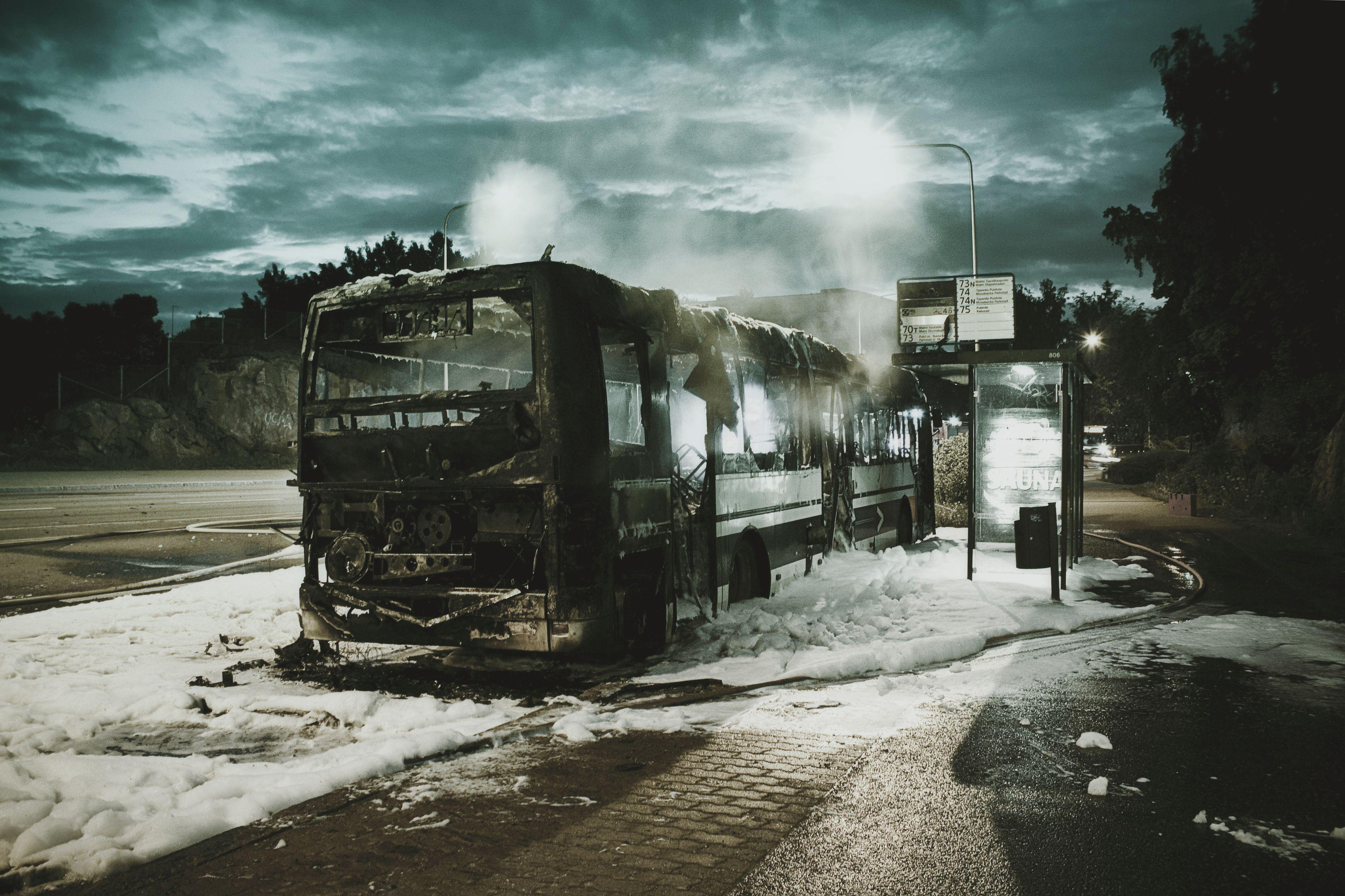 A burnt-out bus with foam and smoke at a suburban street during a rainy night.