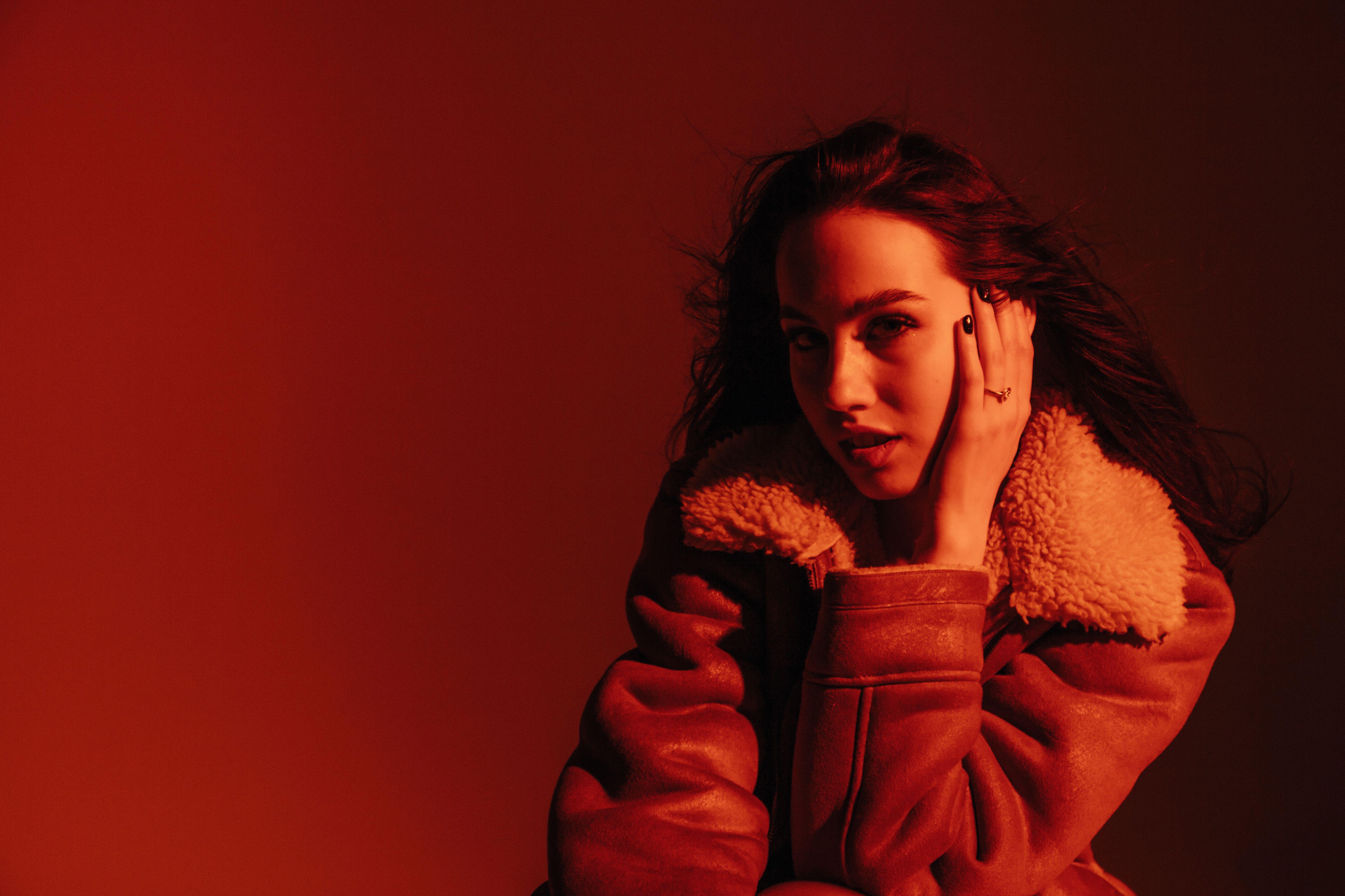 A striking portrait of a woman in a shearling jacket with shadow and red lighting.