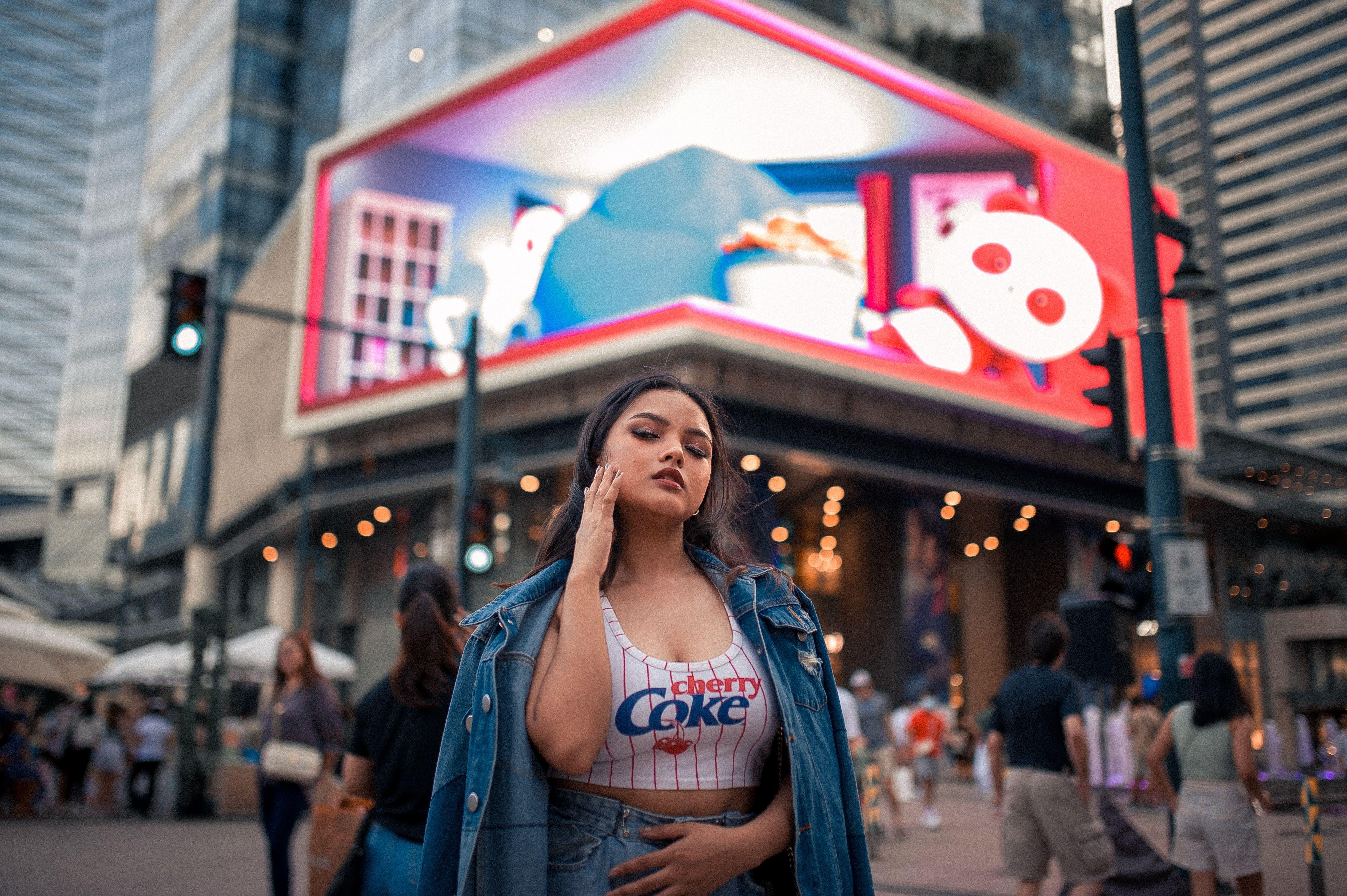 Fashionable young woman posing in an urban city street with colorful billboards in background.