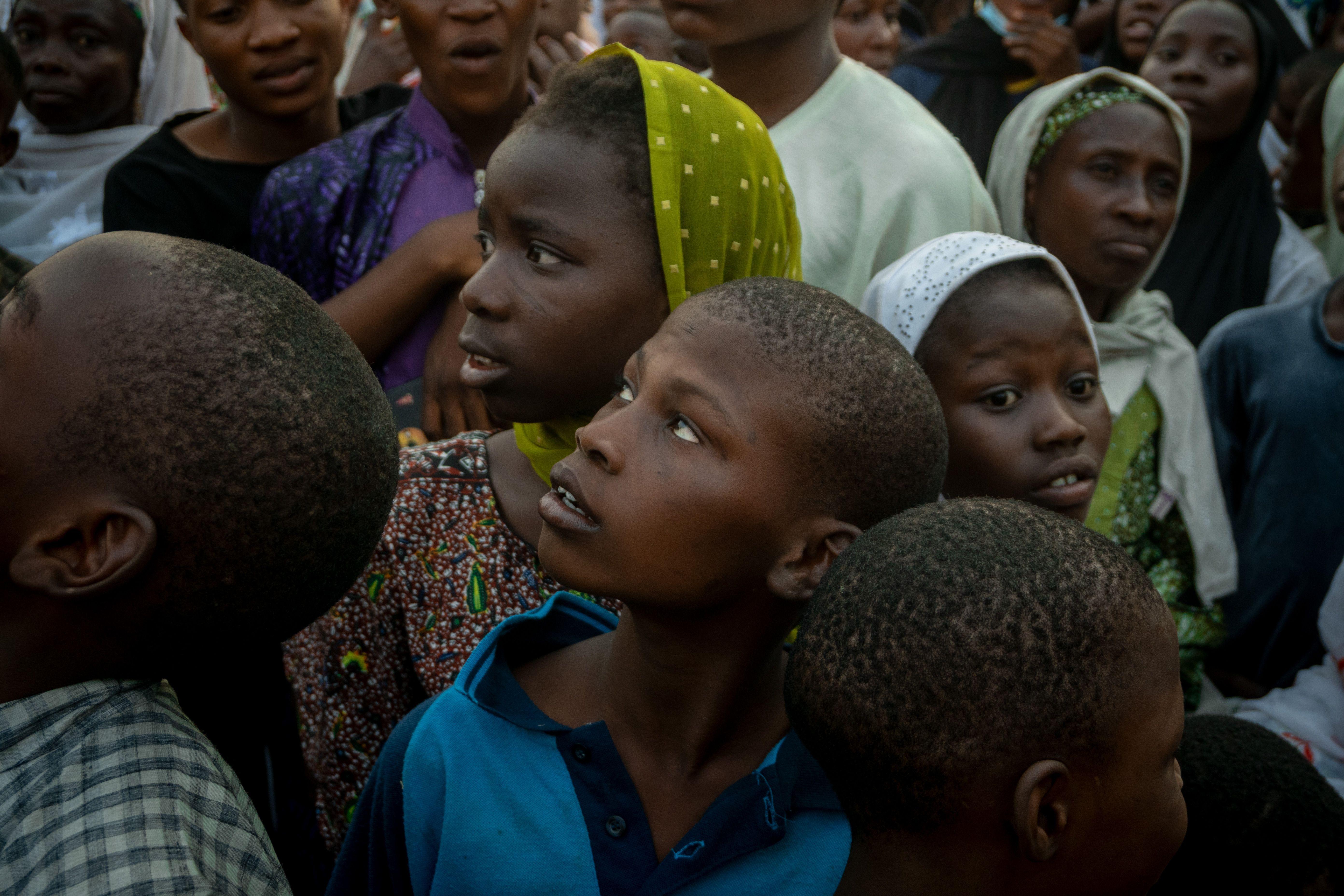 A diverse group of children looking up in curiosity amidst a crowd, evoking a sense of anticipation.