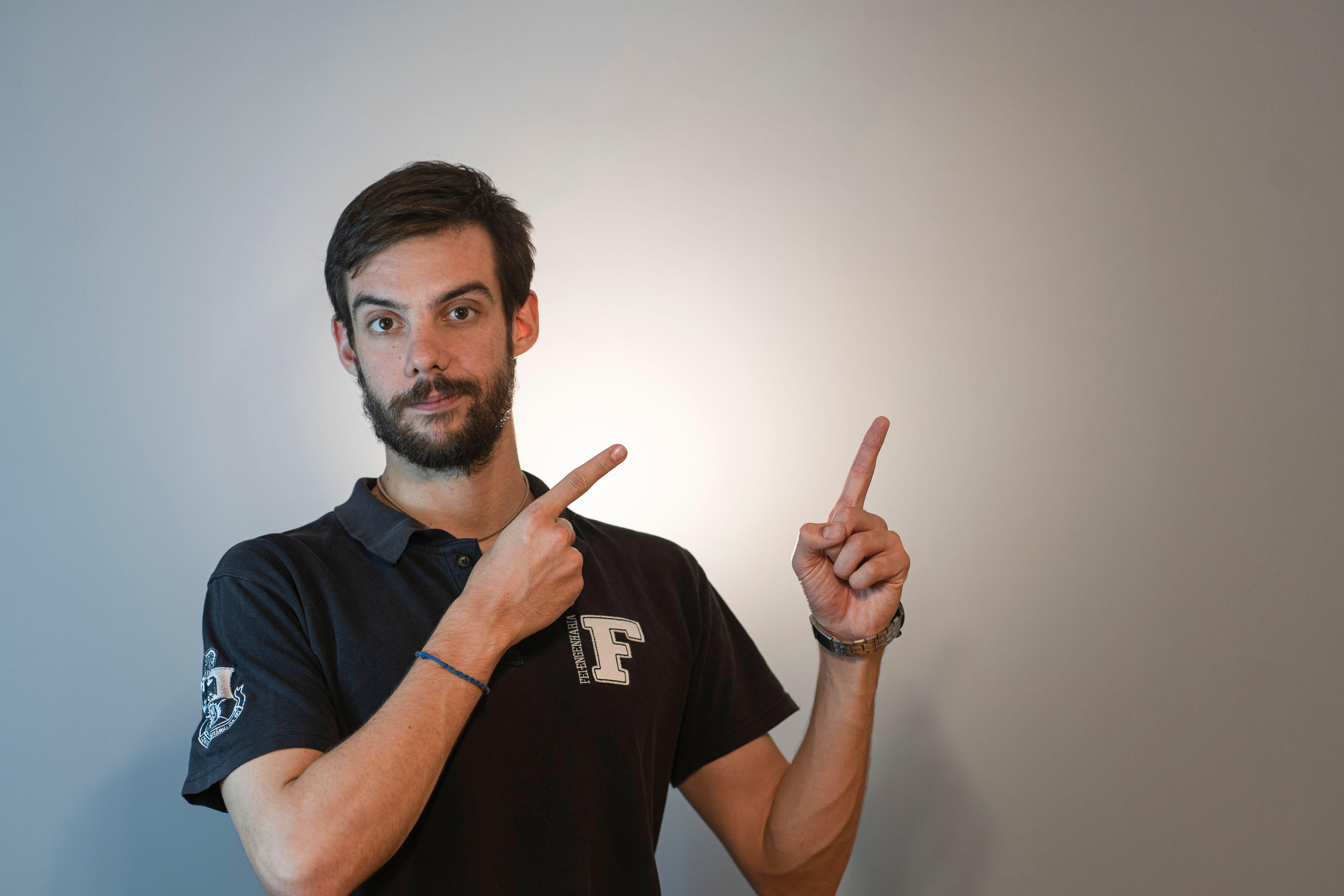 Man with beard and short hair wearing polo shirt pointing upward in studio.