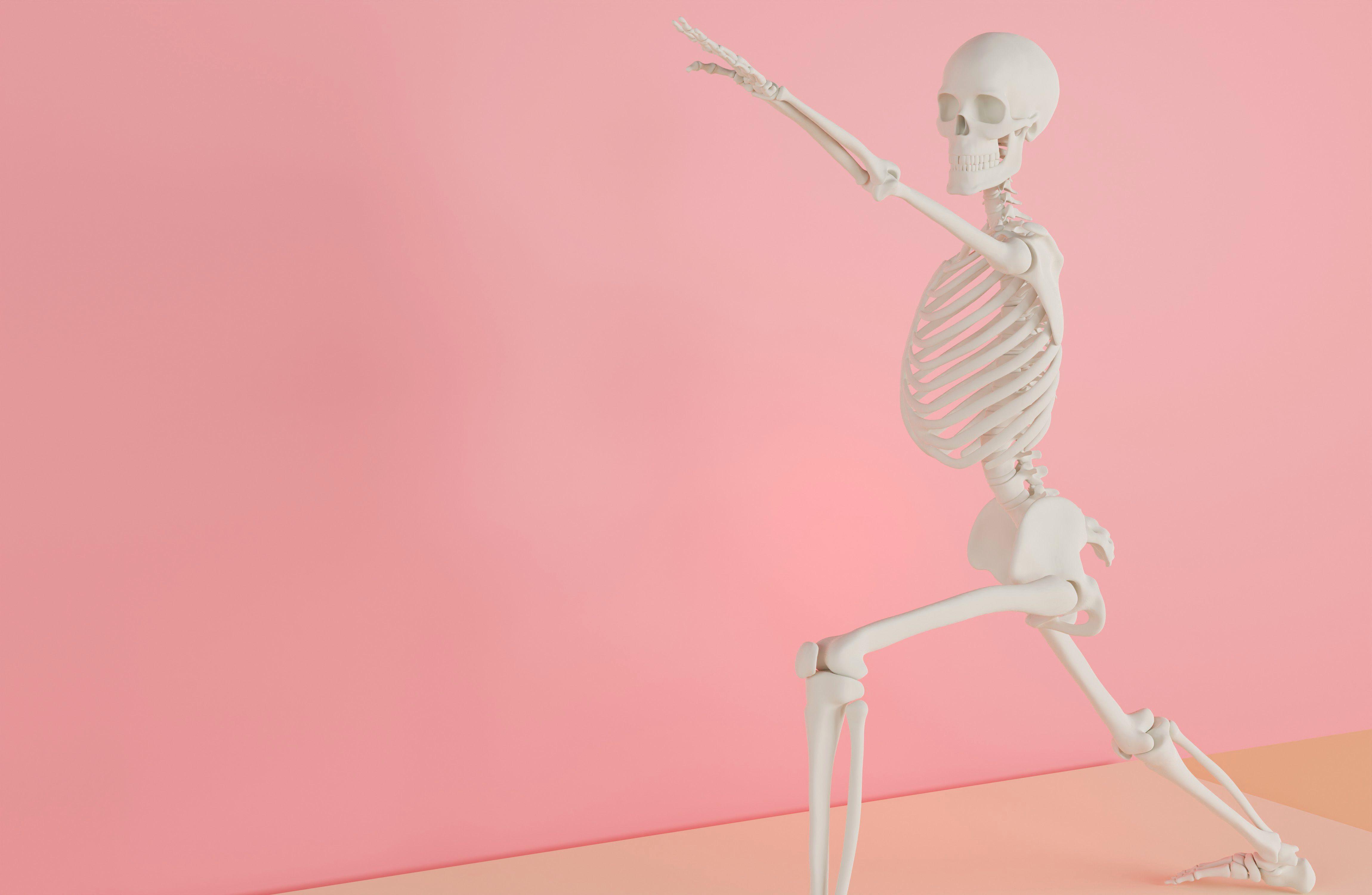 A skeleton model doing a yoga stretch on a pink backdrop, symbolizing fitness and anatomy.
