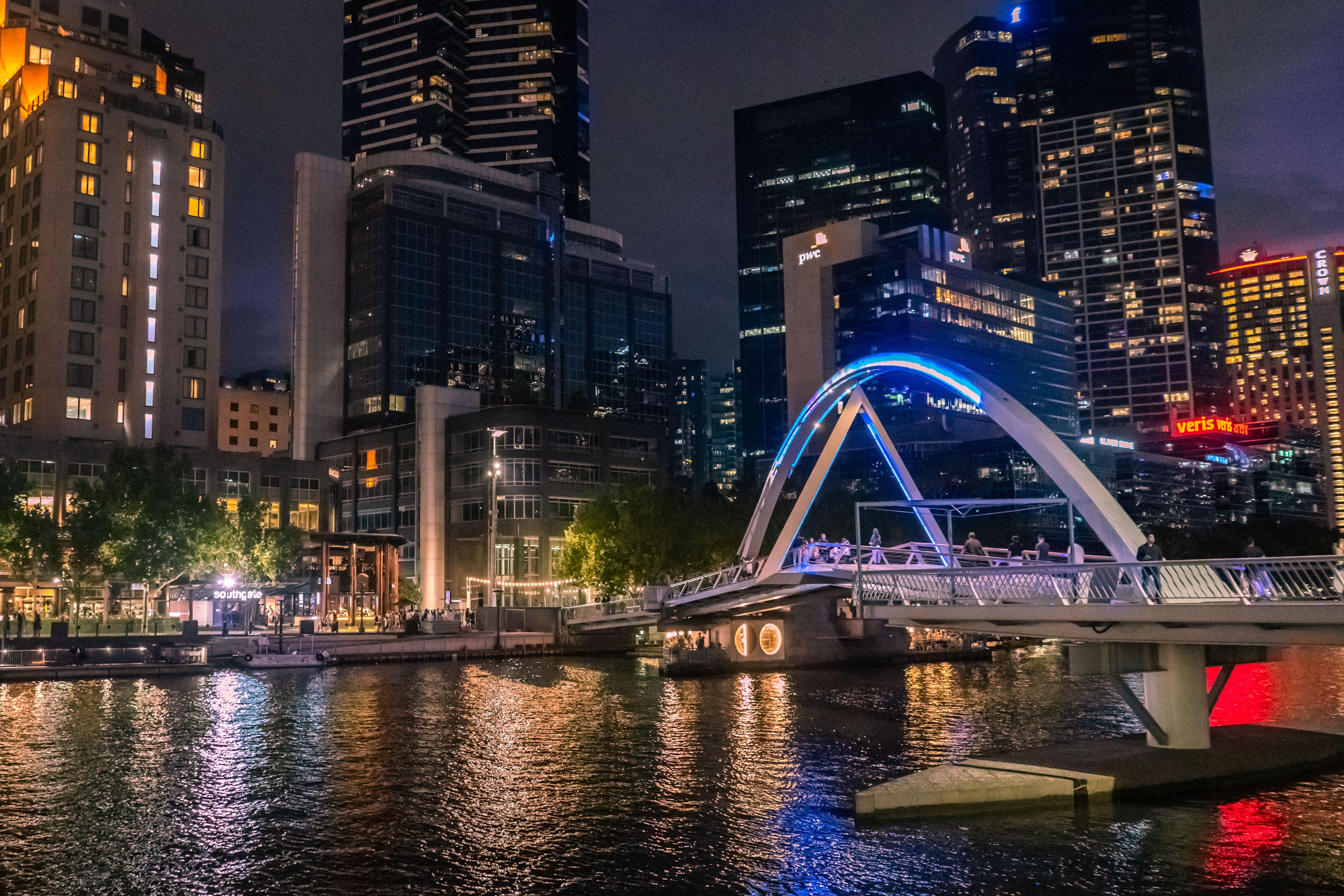 Illuminated Evan Walker Bridge crossing Yarra River in Melbourne's skyline at night.