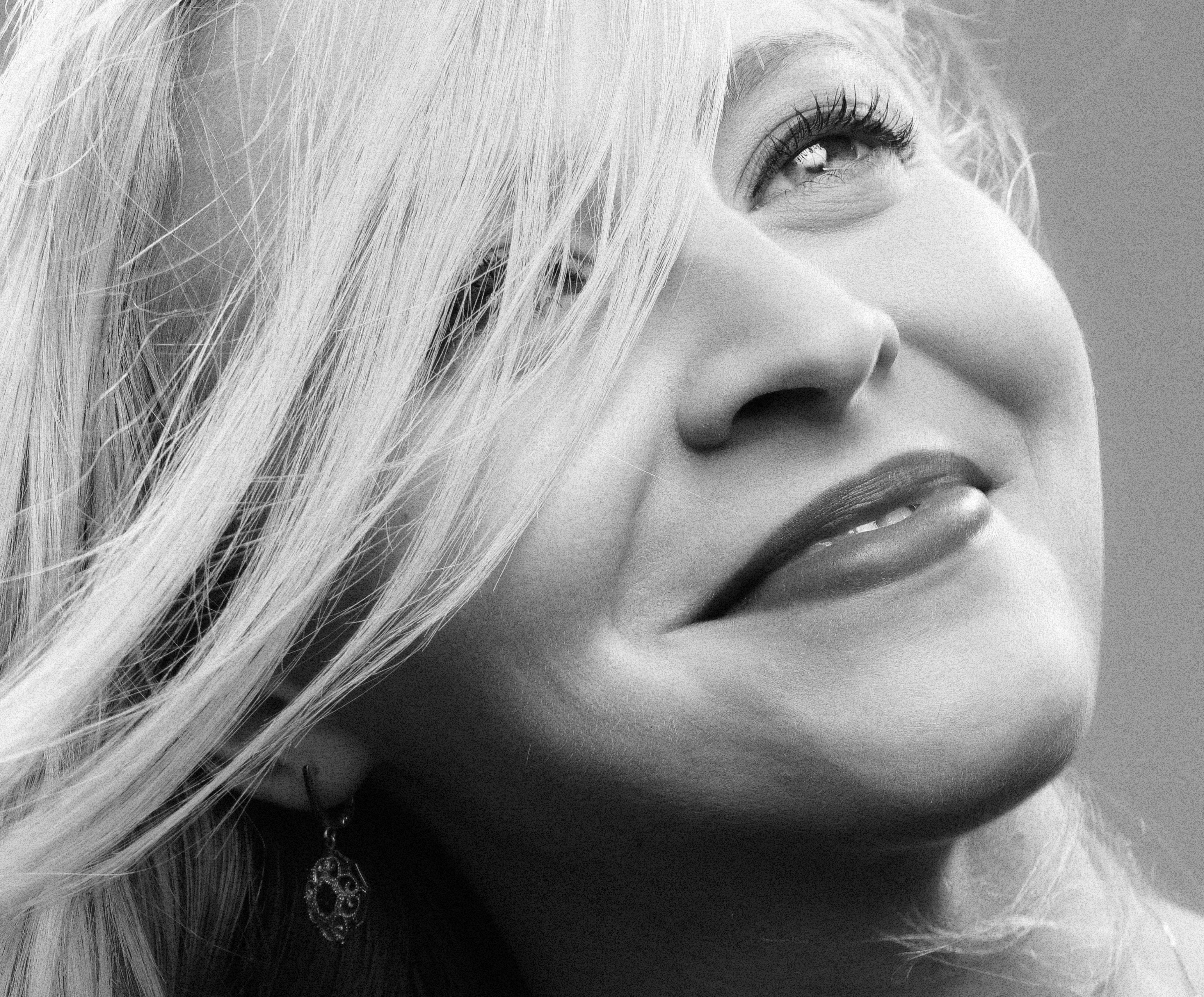 Close-up black and white portrait of a smiling woman with flowing hair, exuding elegance.
