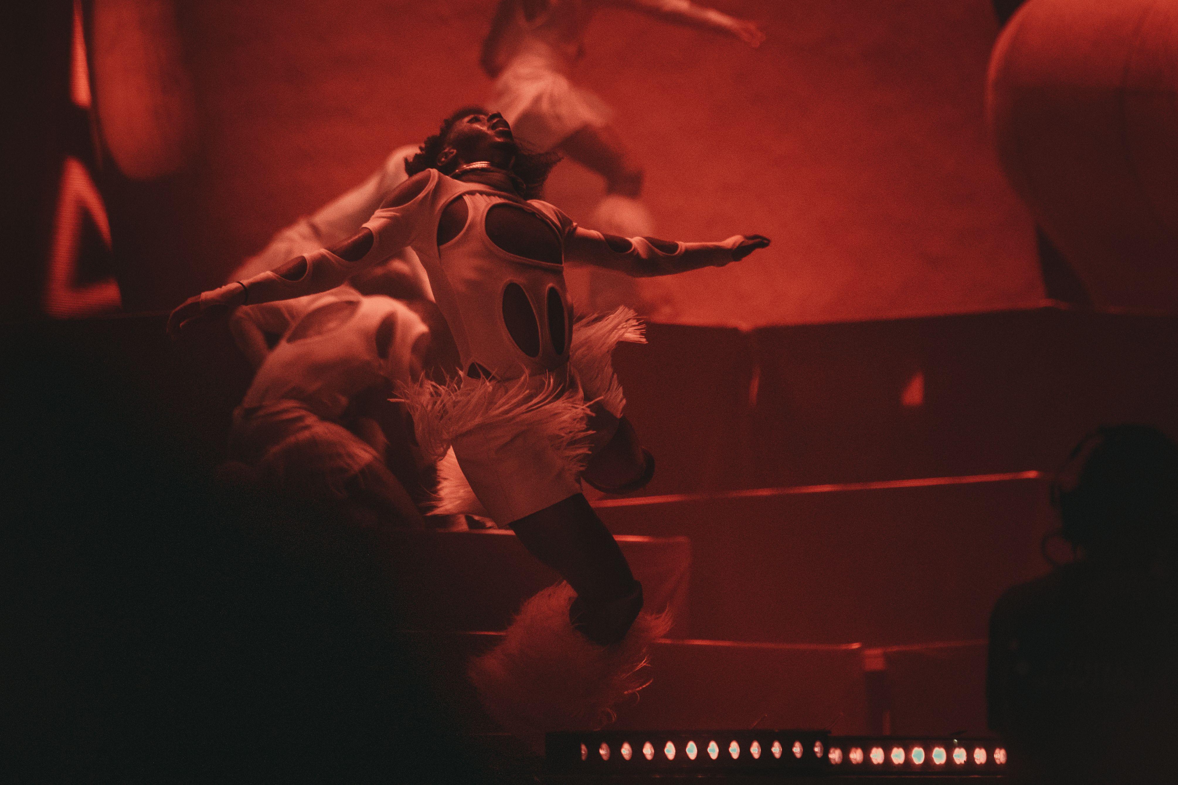 Energetic dancers performing on stage in striking red lighting and creative costumes.