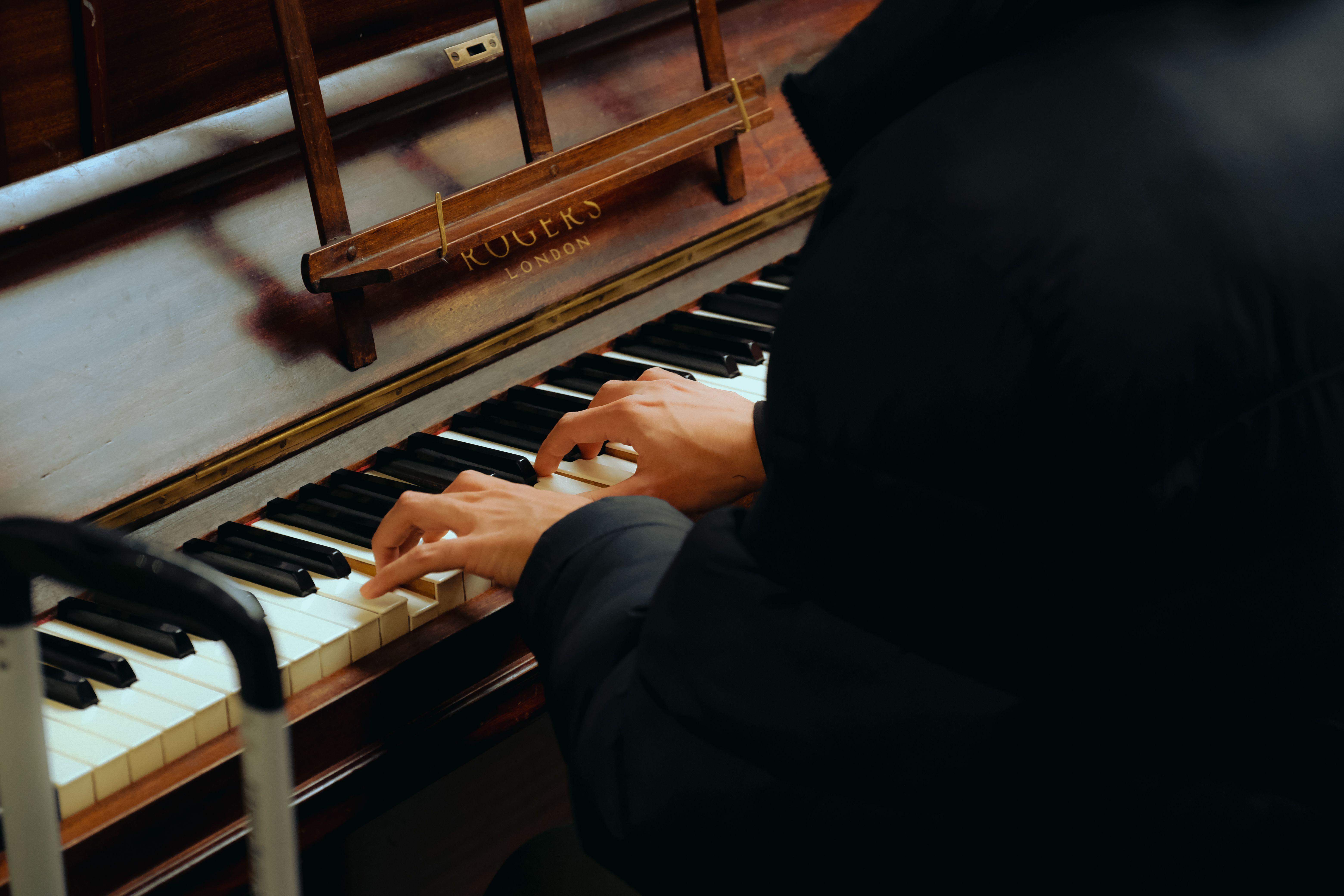 Close-up of hands playing a Rogers London upright piano indoors.