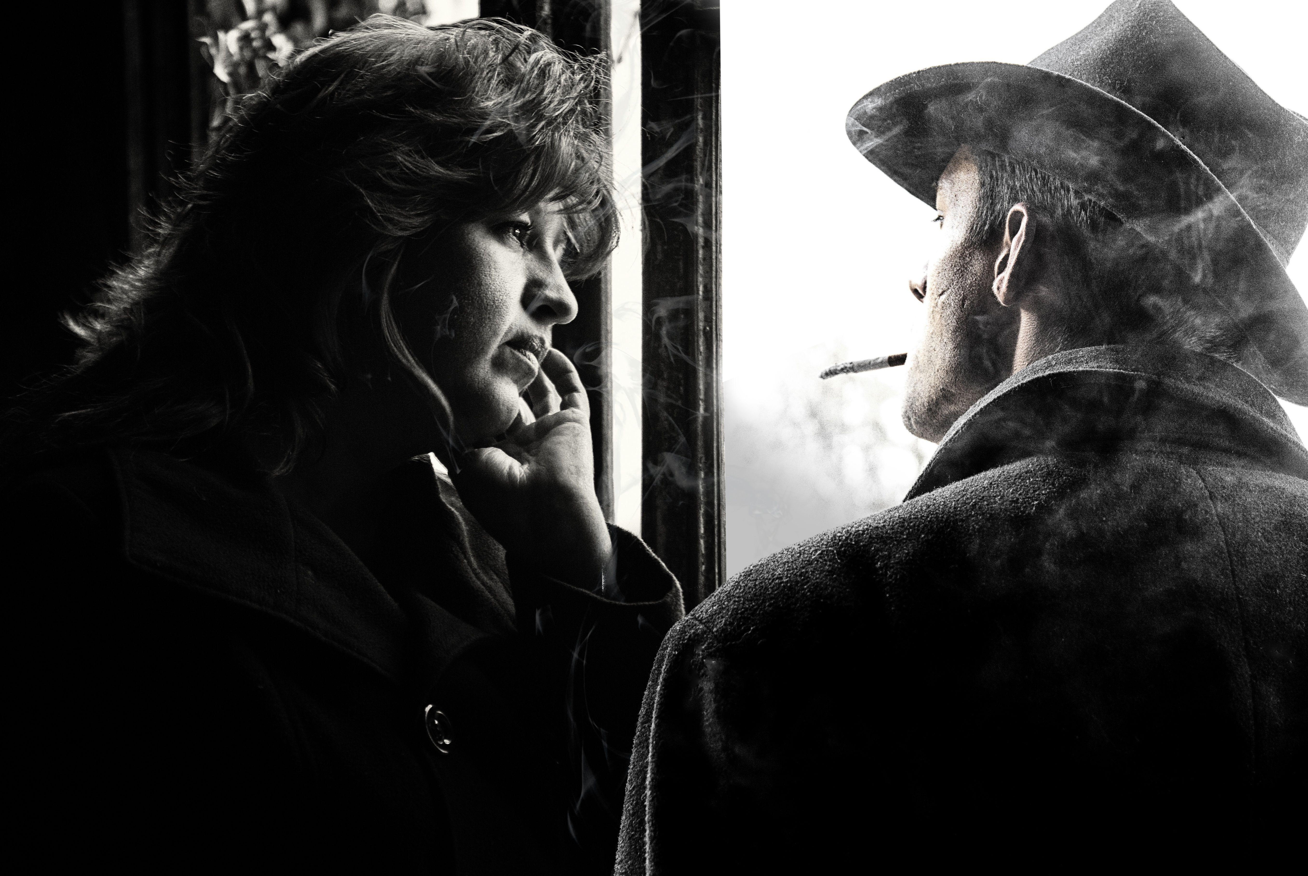 A contemplative couple in a black and white photo, with a cigarette and window adding to the mood.