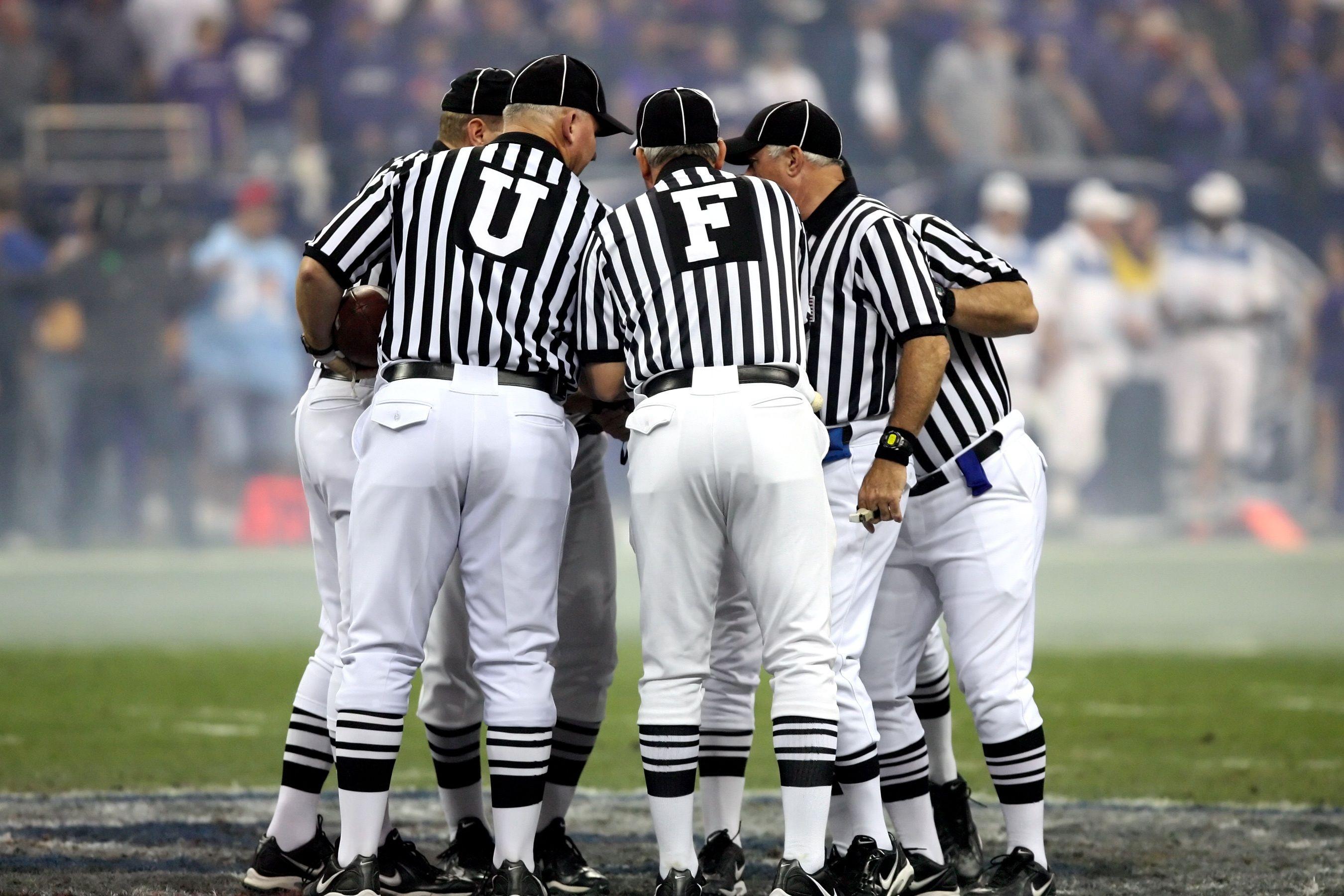 Group of sports officials in striped uniforms discussing on a football field.