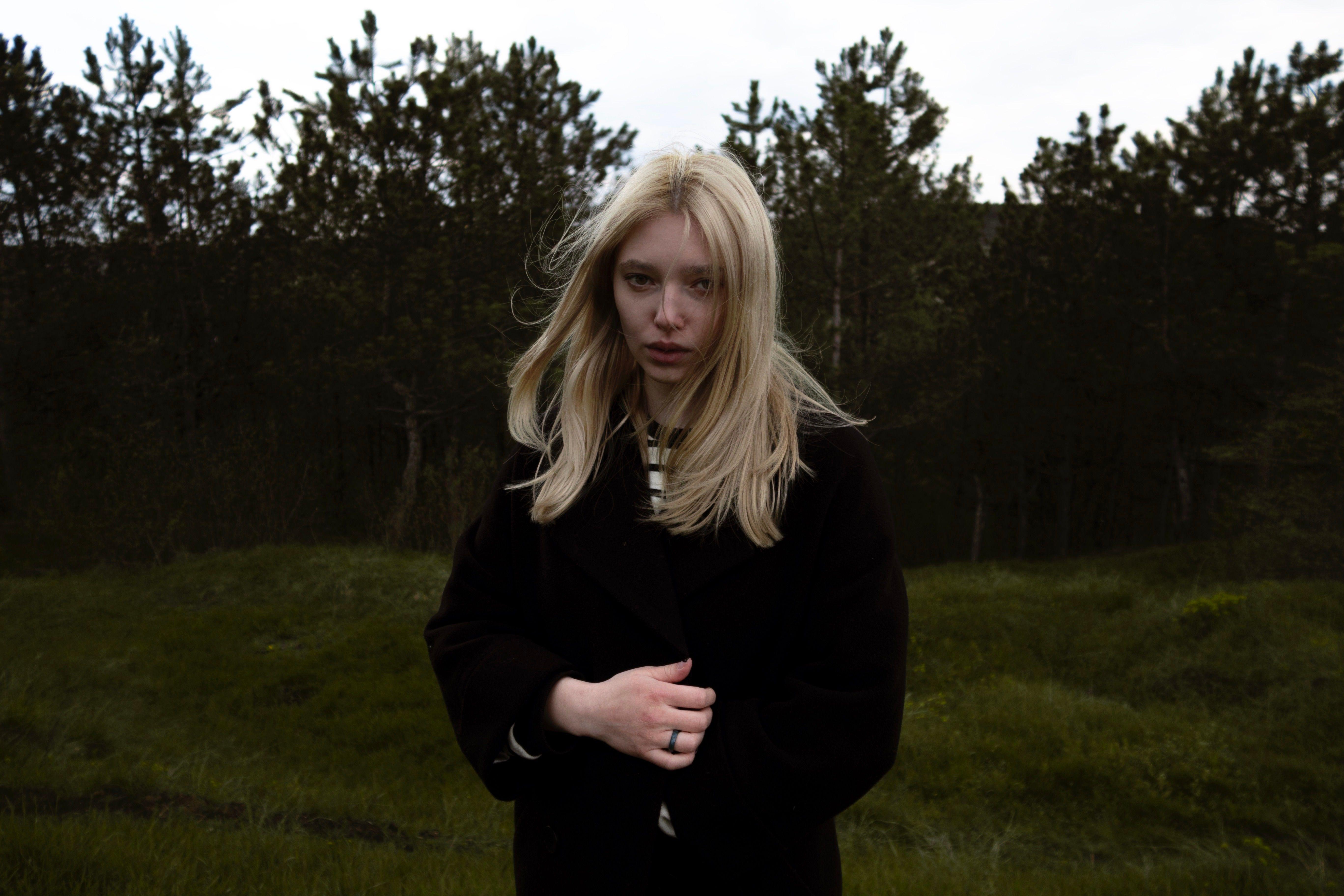 Portrait of a young woman with blonde hair in a black coat outside.