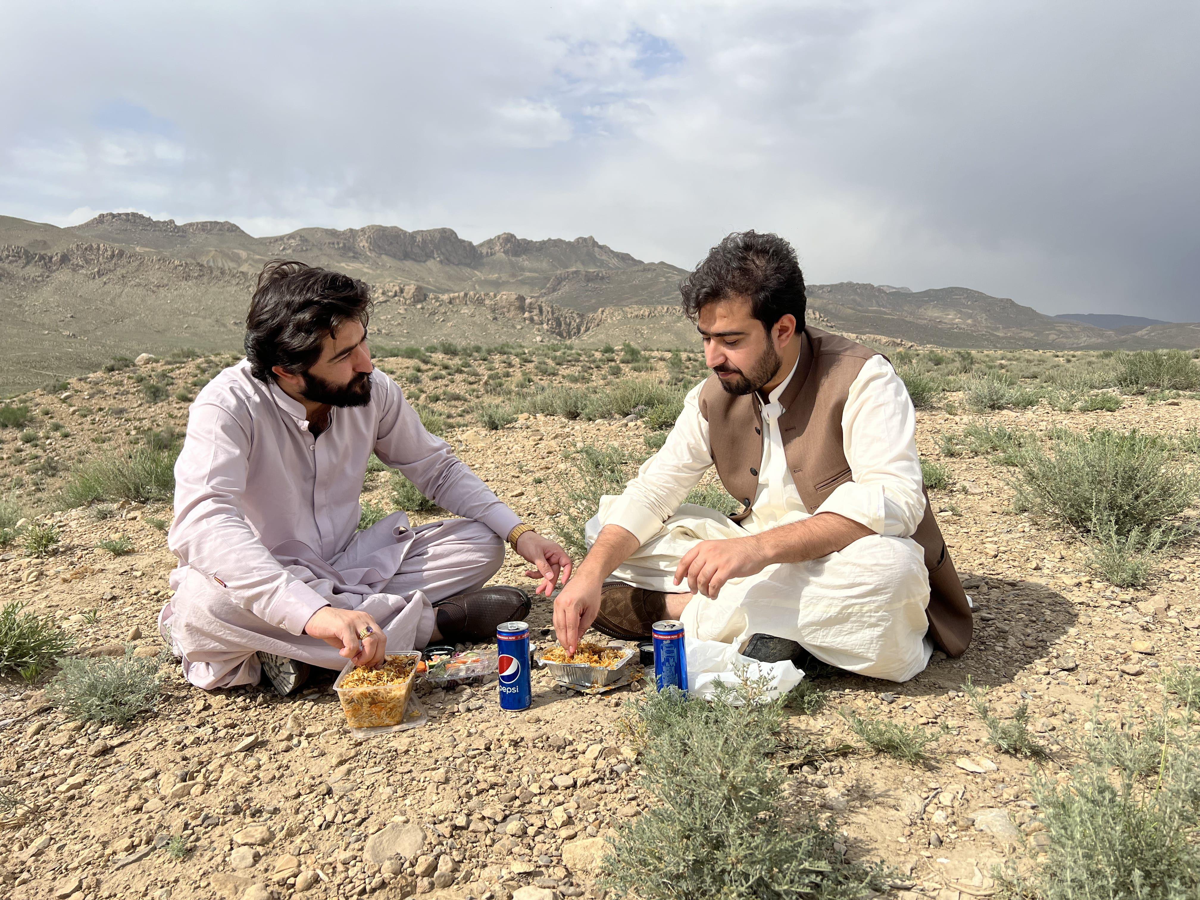 Two men sharing a meal outdoors in Quetta, Balochistan with scenic mountain views.