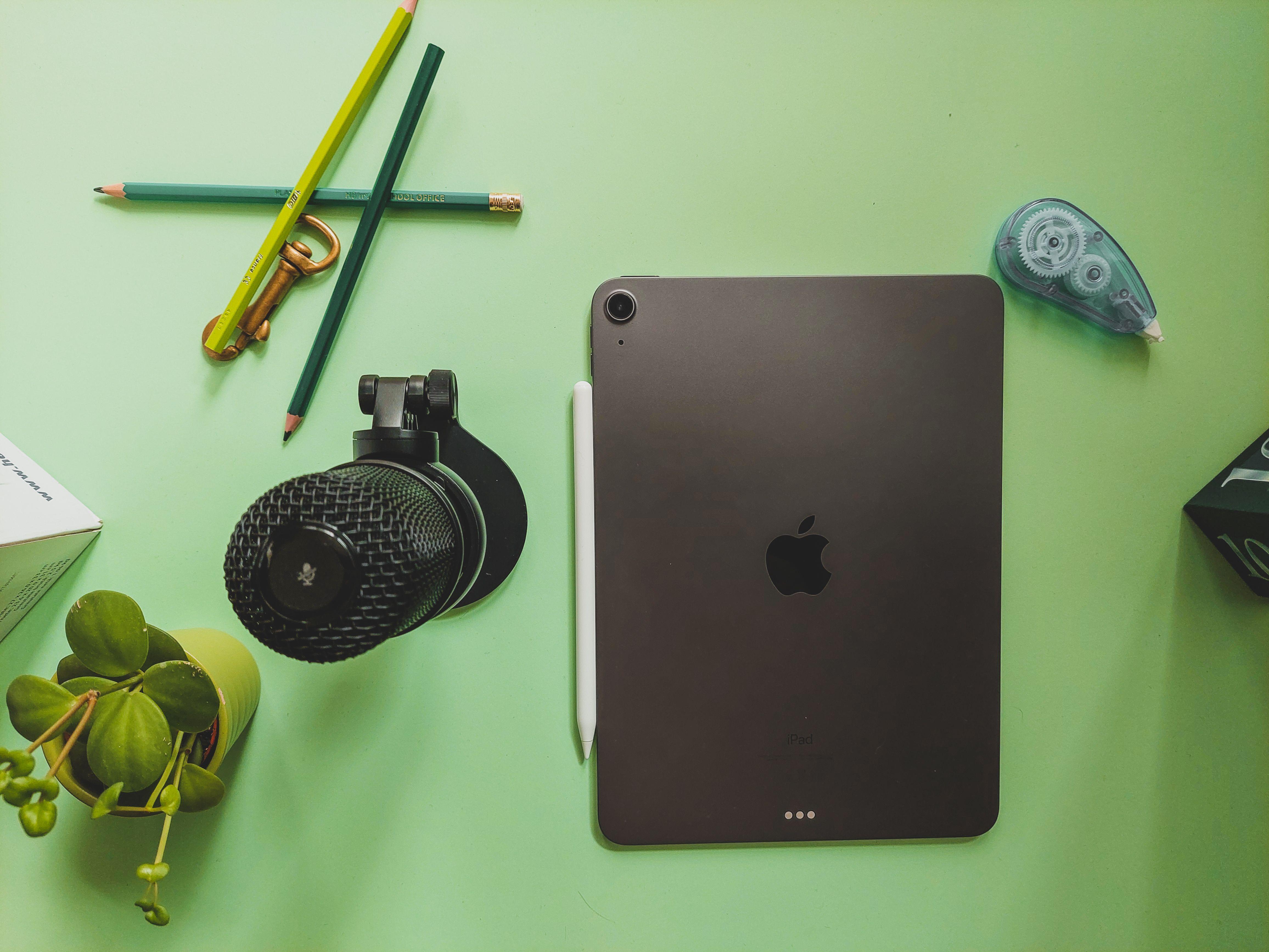 Flat lay of a workspace featuring a tablet, microphone, and stationery on a green desk.