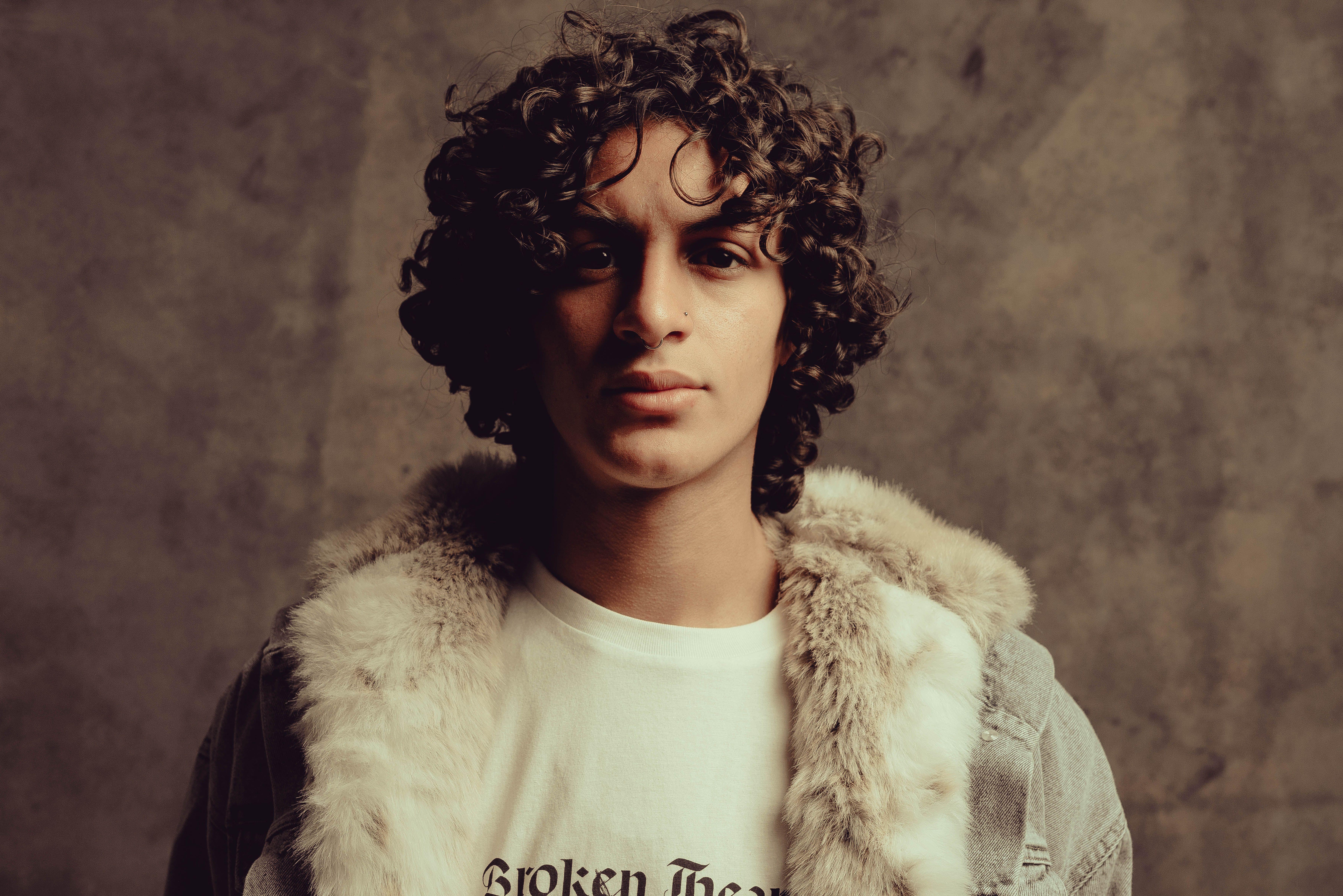 Stylish portrait of a young man with curly hair wearing a fur jacket in a studio setting.