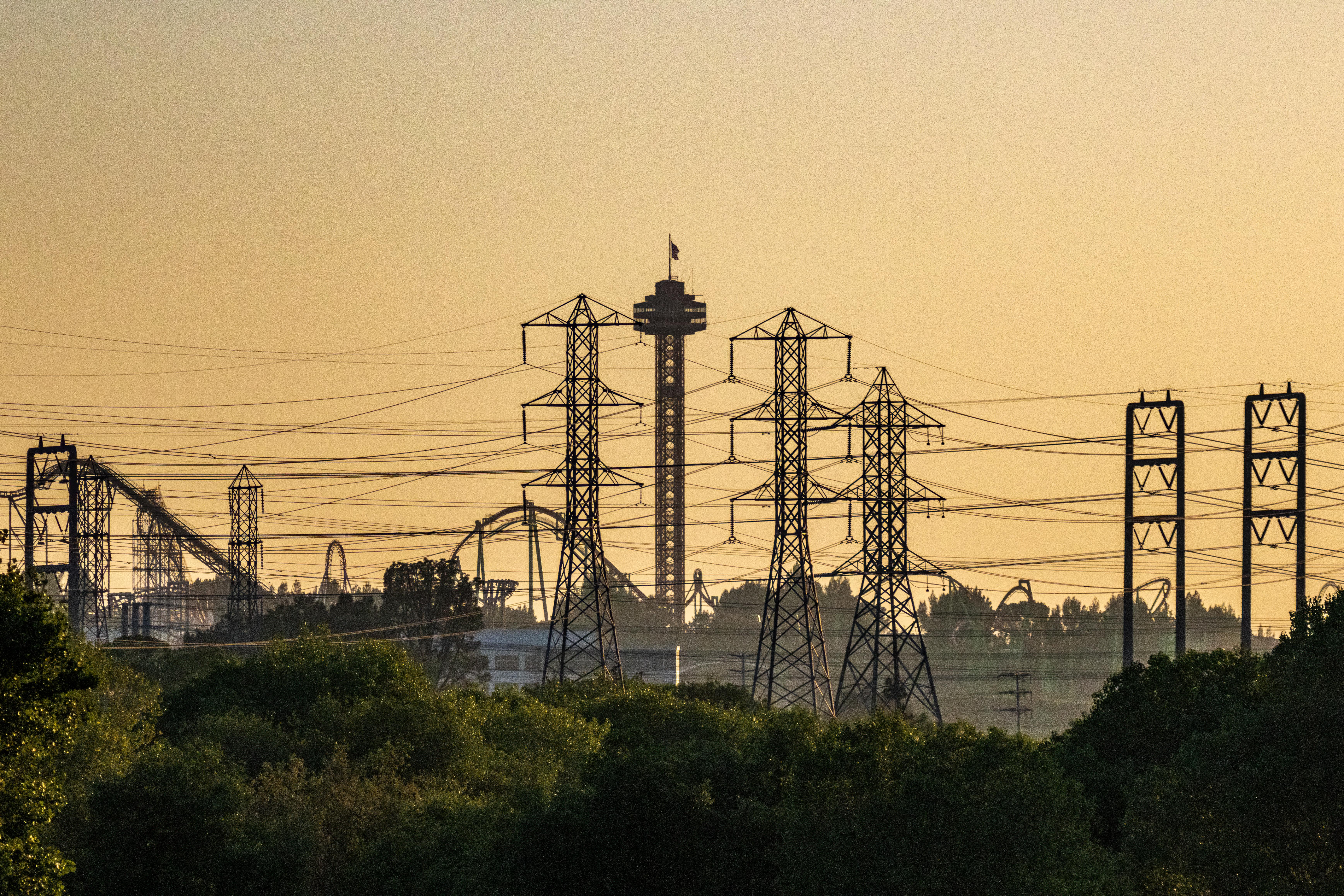 Silhouette of power lines and an amusement park at sunset with clear sky.