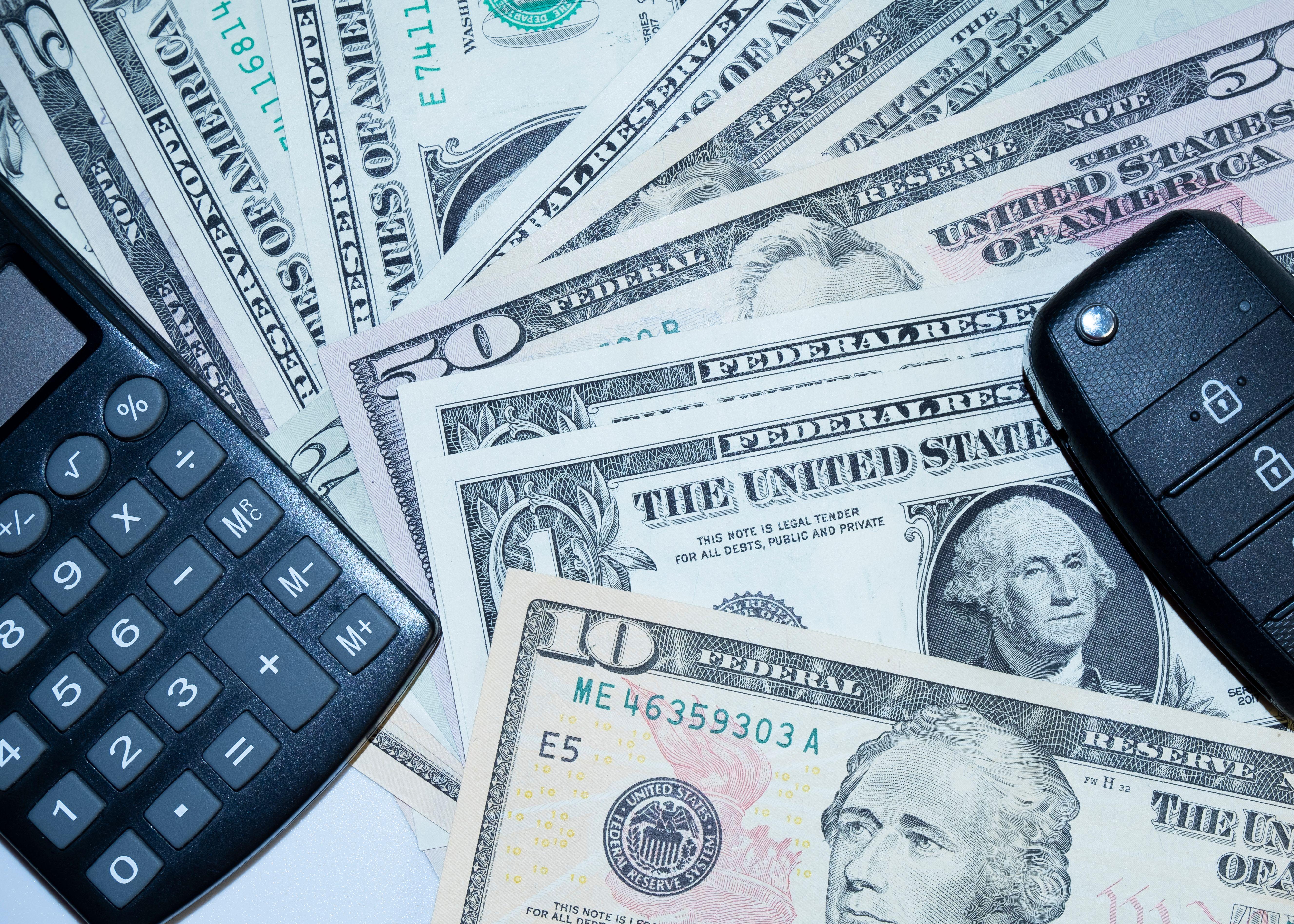 US dollars, calculator, and car keys representing finance and investment tools.