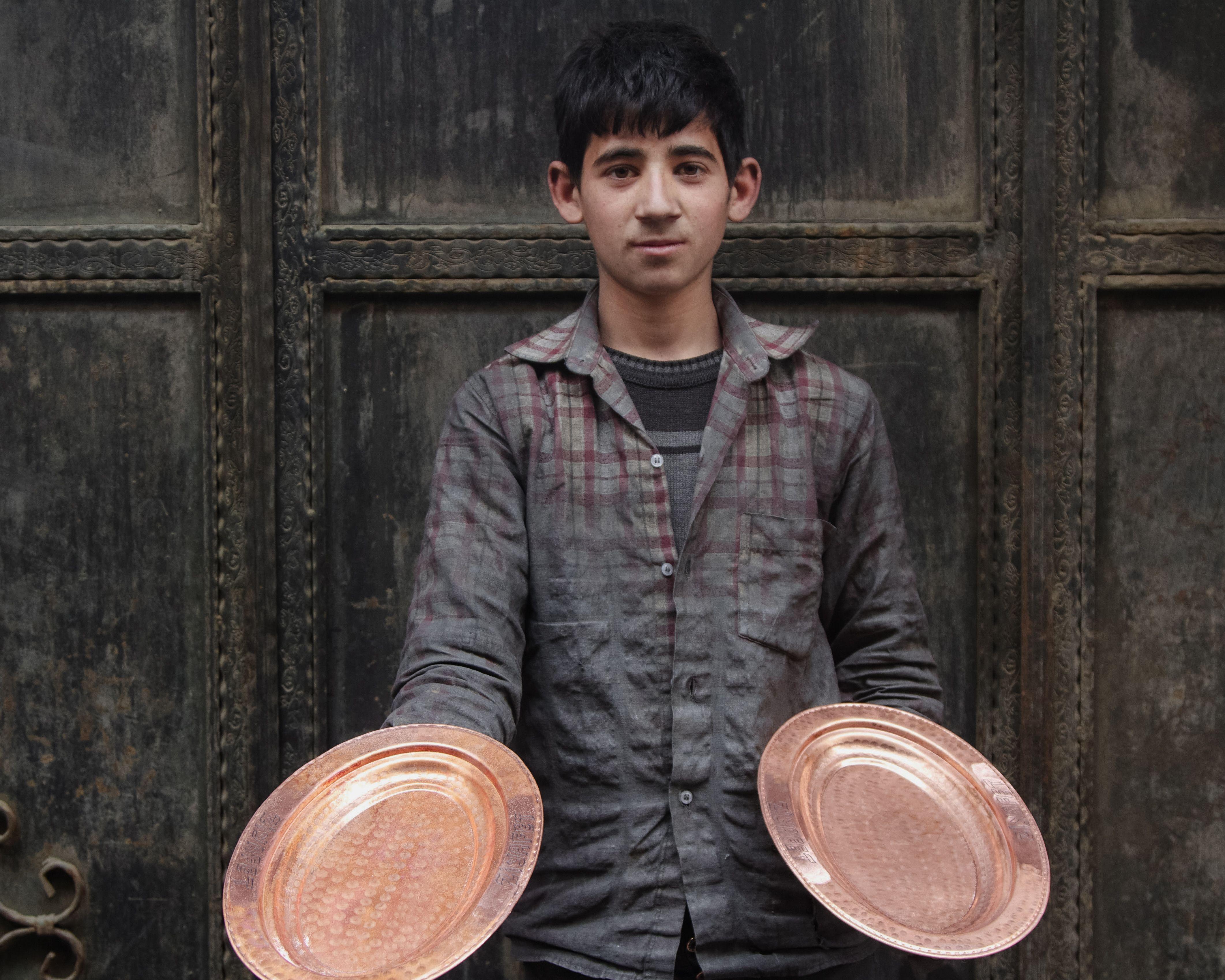 A young artisan proudly displaying handcrafted copper plates, showcasing traditional craftsmanship.