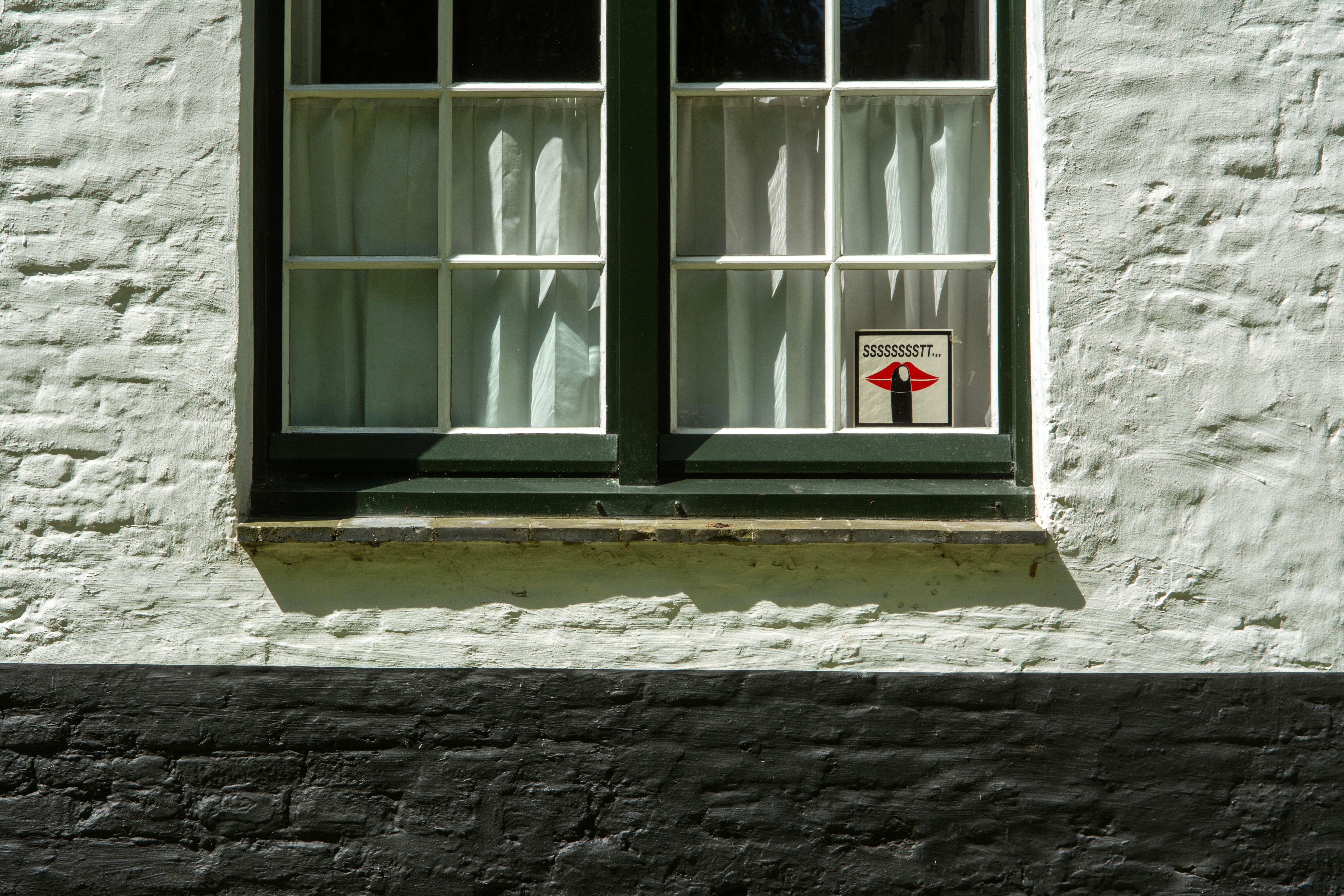 Close-up of a traditional window in Brugge with a unique 'Shhh' sign.