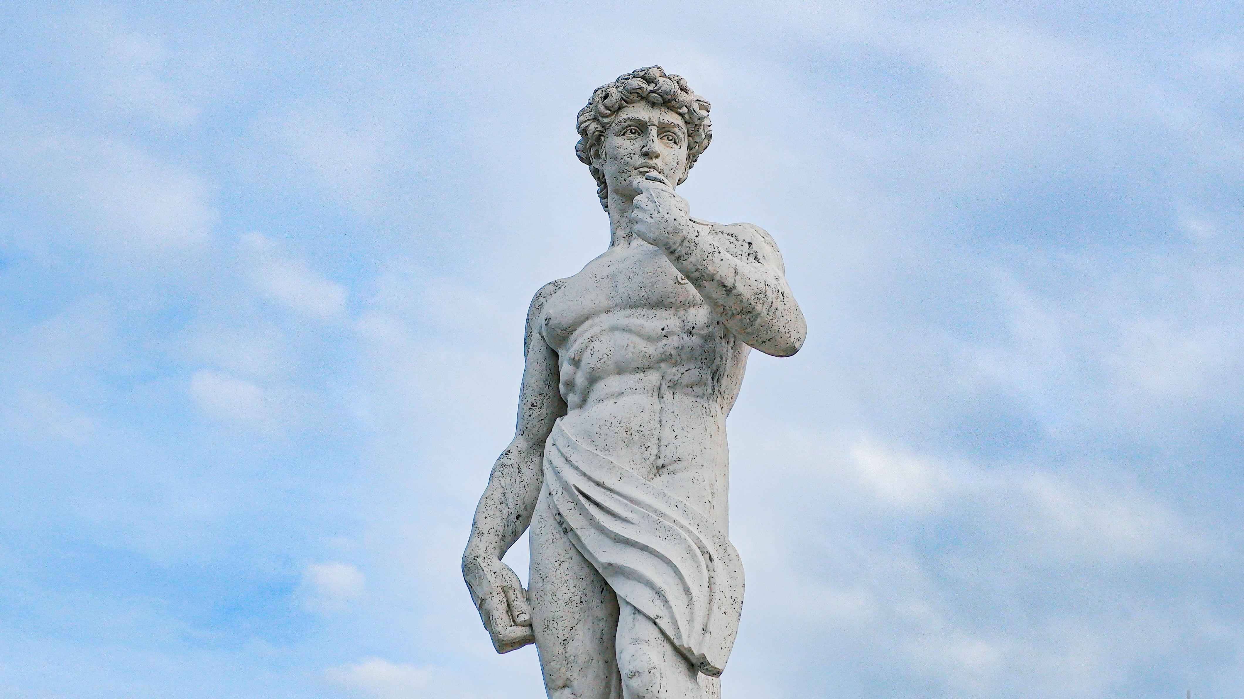 Low angle view of Michelangelo's David sculpture under a blue sky, showcasing its classical art beauty.