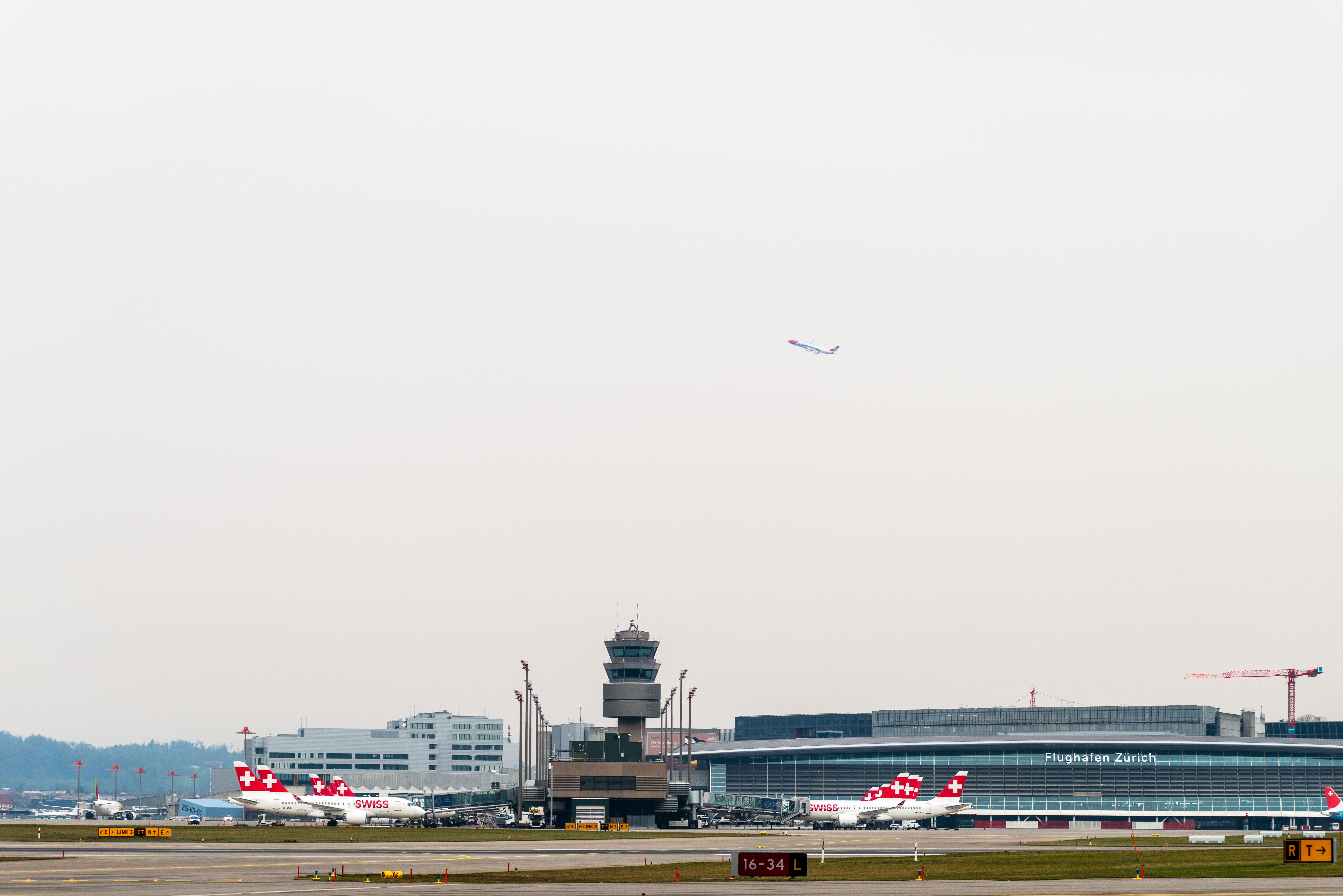 Swiss airplanes at Zurich Airport with control tower and terminal in background.