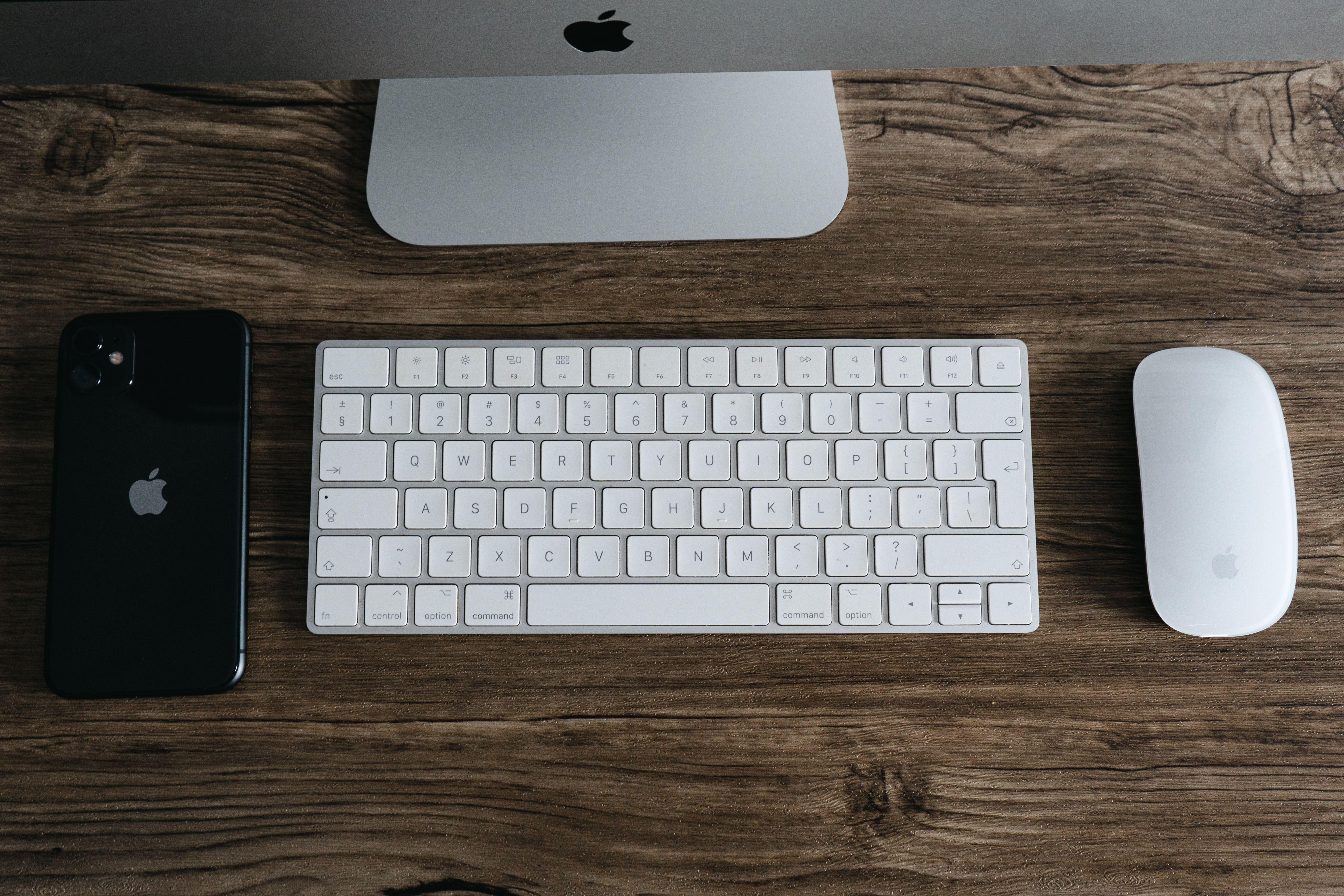 A minimalist workspace featuring a smartphone, keyboard, and mouse on a wooden desk.