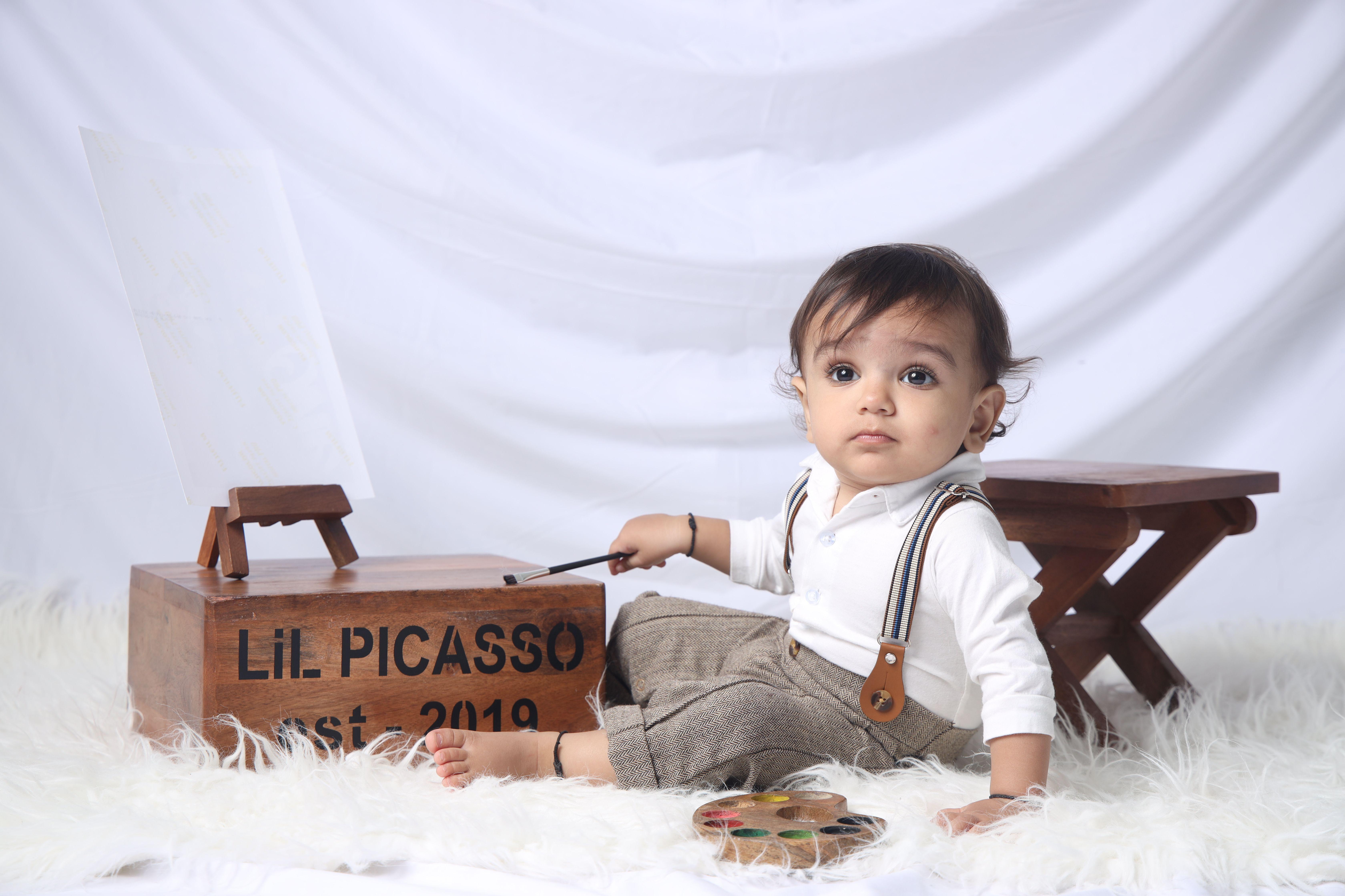 Adorable baby dressed as an artist playing with a paintbrush and easel in a cozy setting.