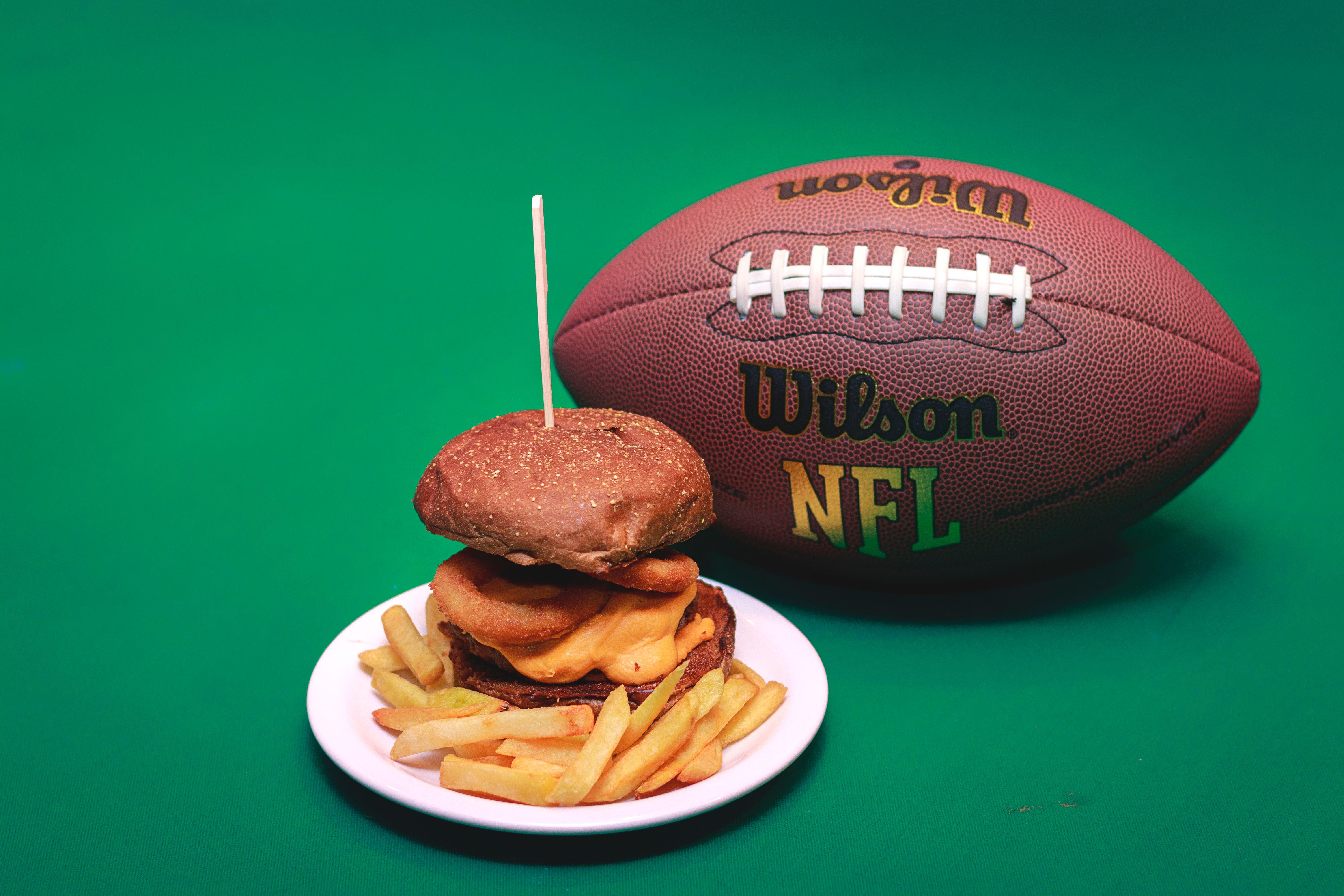 A cheeseburger and fries on a plate with a Wilson NFL football on a green background.