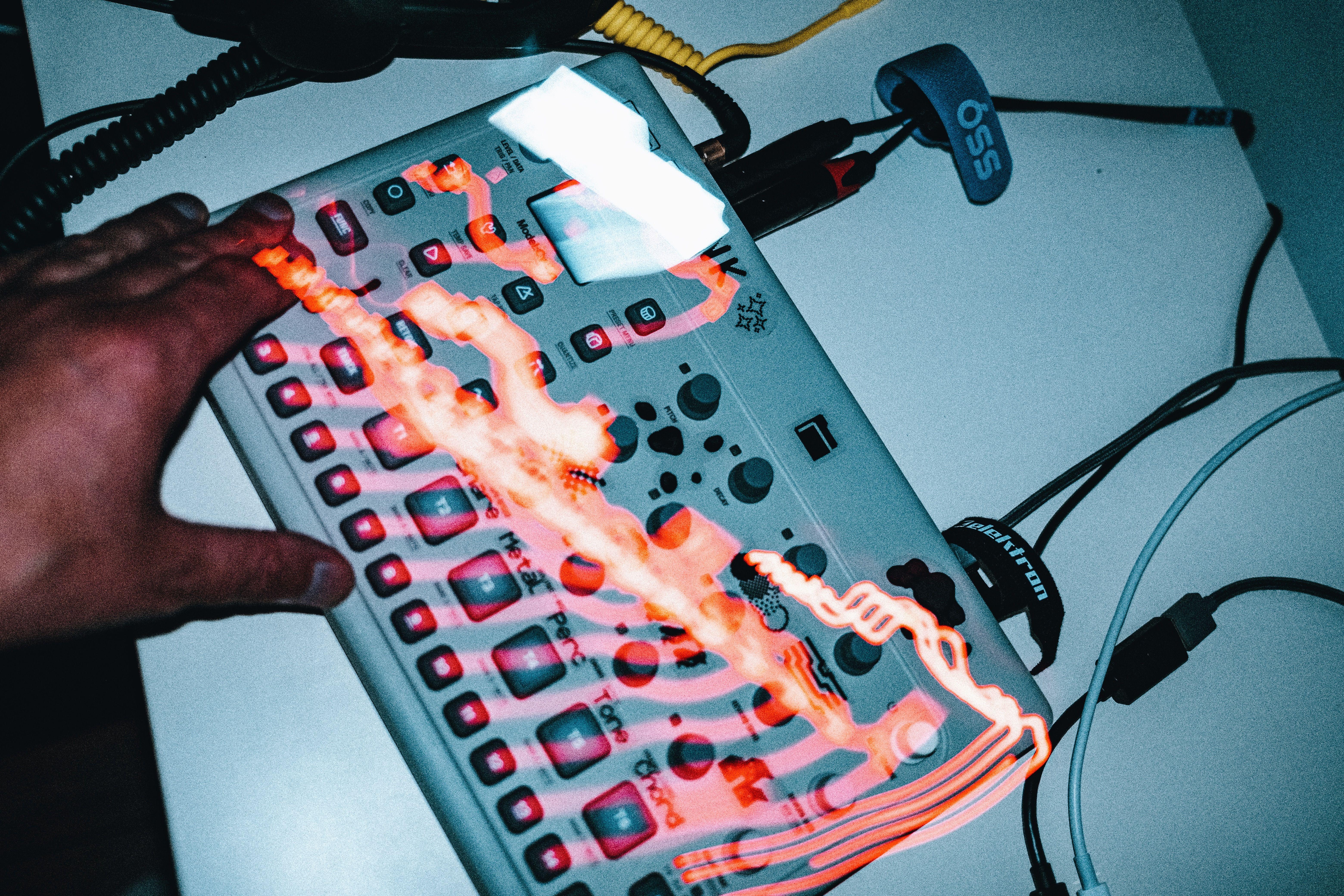 A close-up of a hand on an electronic music device with glowing lights and cables. Perfect for music and technology themes.