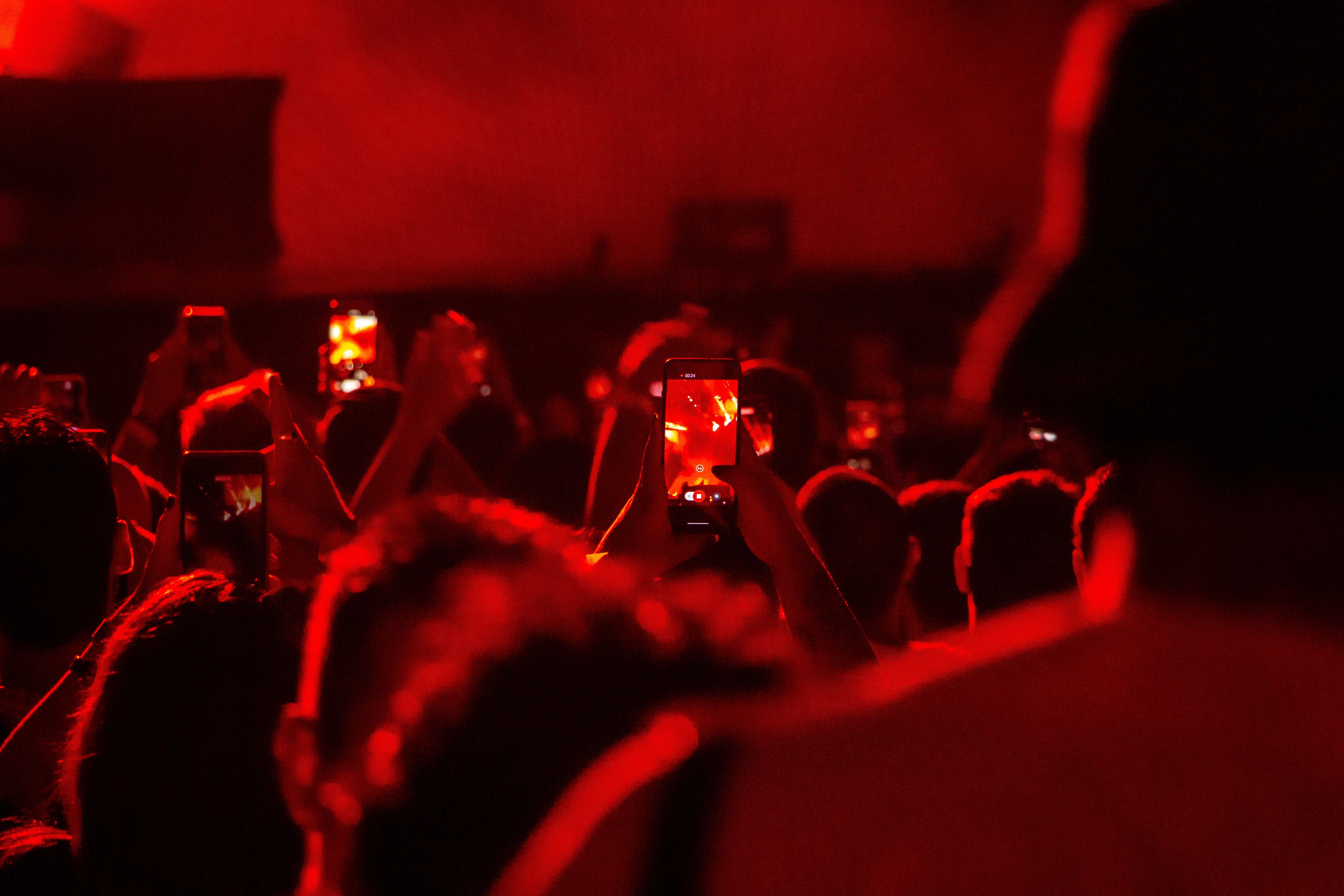 Concert attendees in São Paulo capturing performances with smartphones in a vivid red atmosphere.