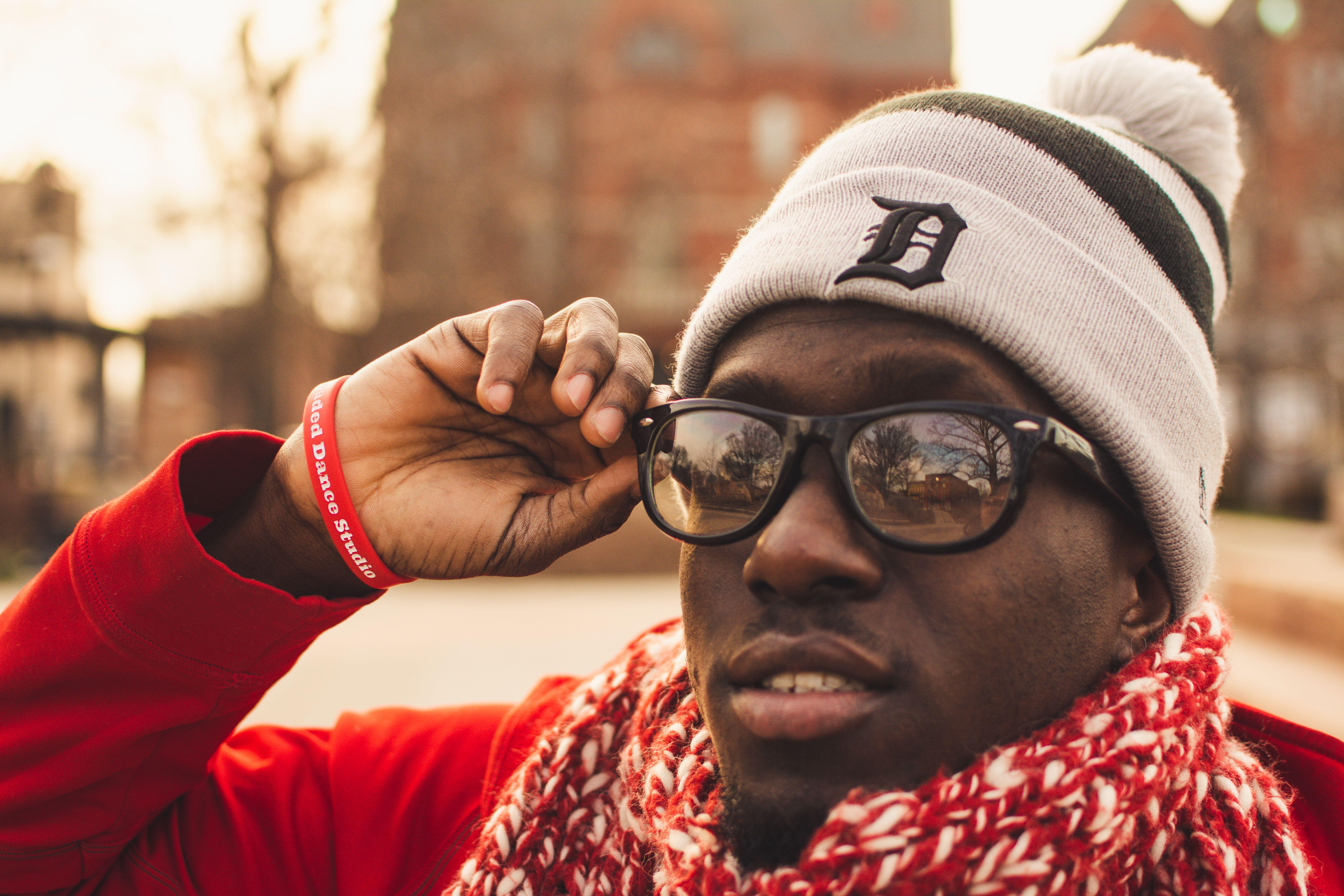 Close-up portrait of a man wearing a scarf and beanie with sunglasses outdoors, exuding a warm winter vibe.