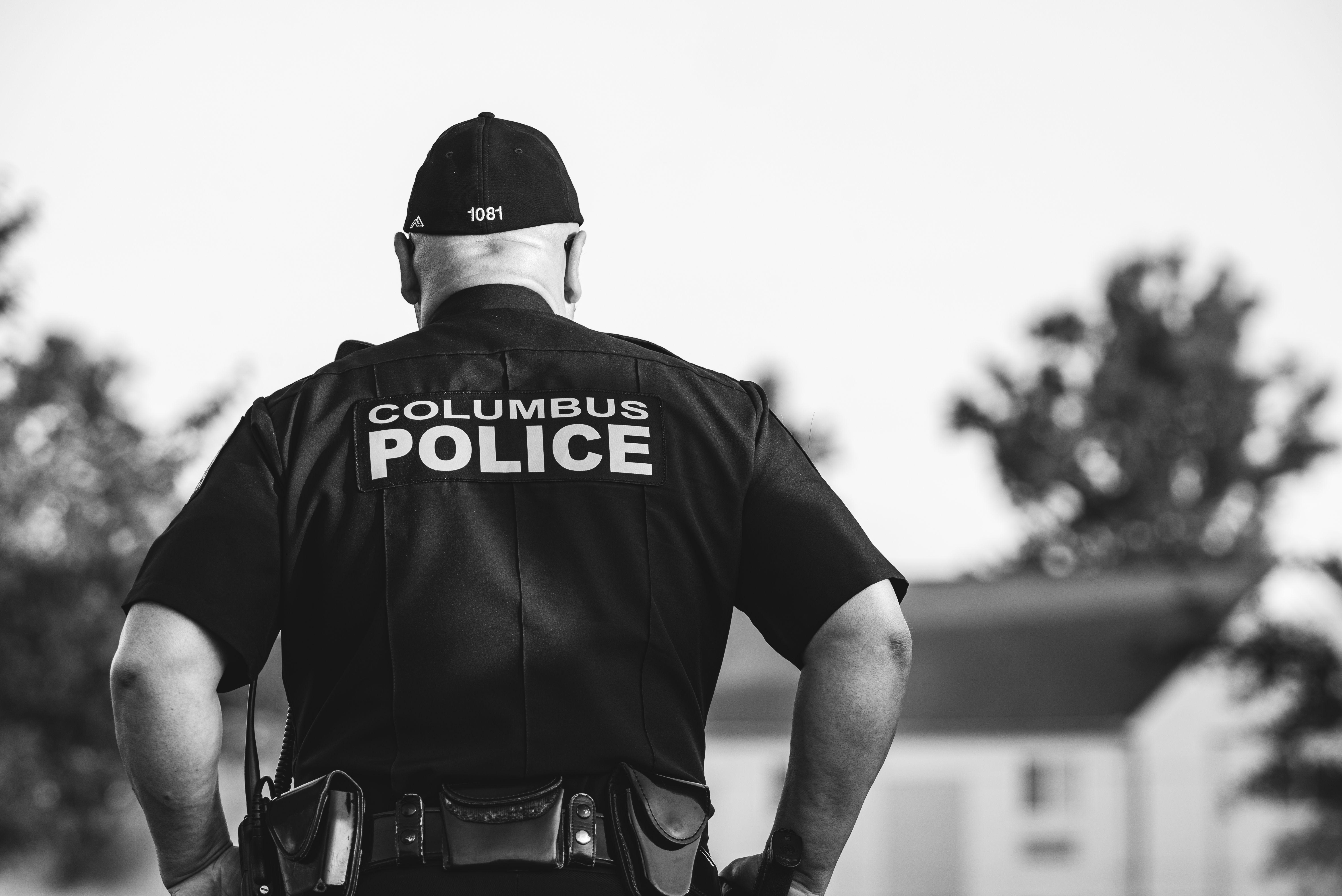 Black and white photo of a police officer in uniform from Columbus, outdoors, in focus.
