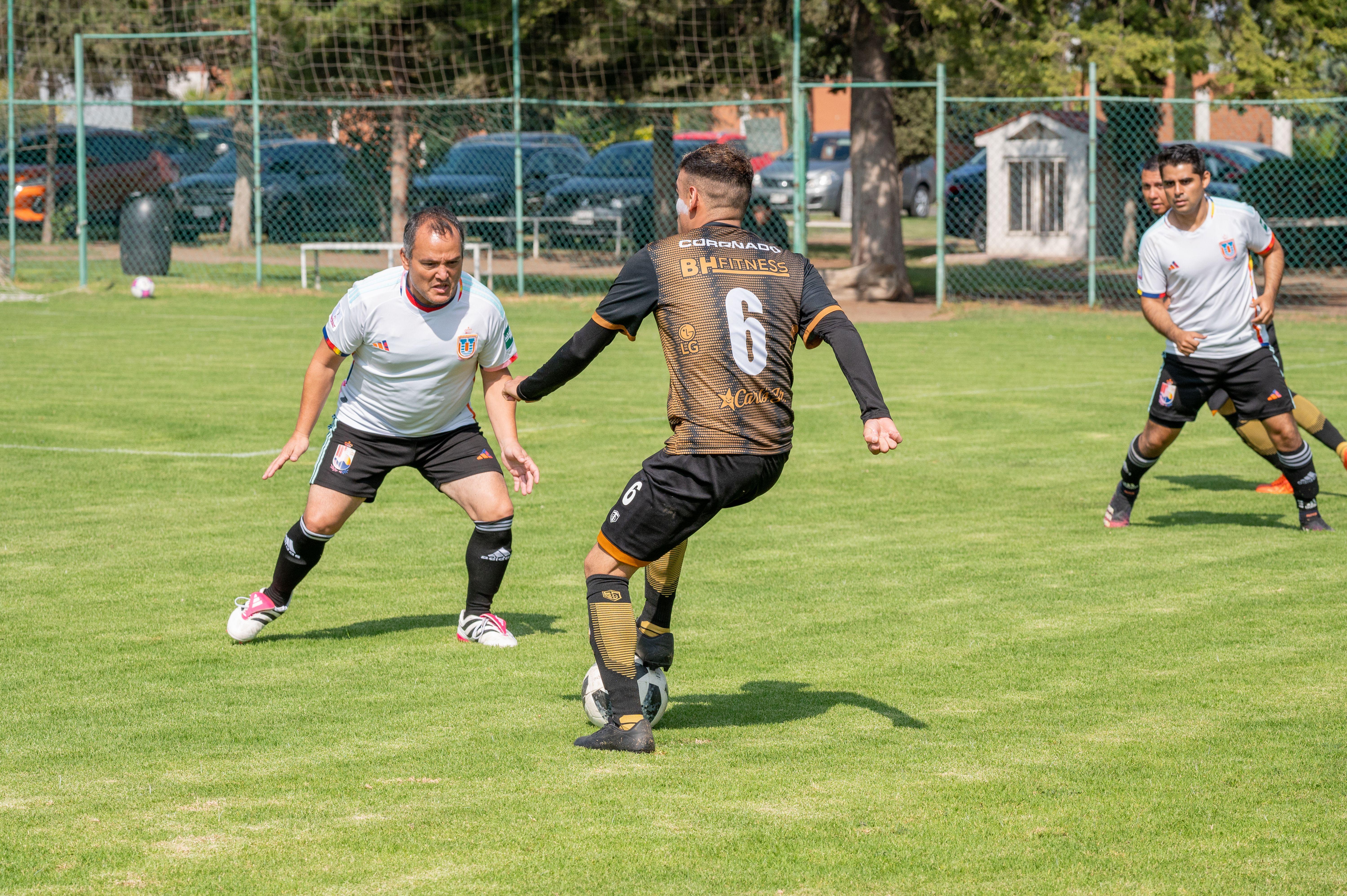Adult men playing a friendly soccer game on a grassy field under clear skies.