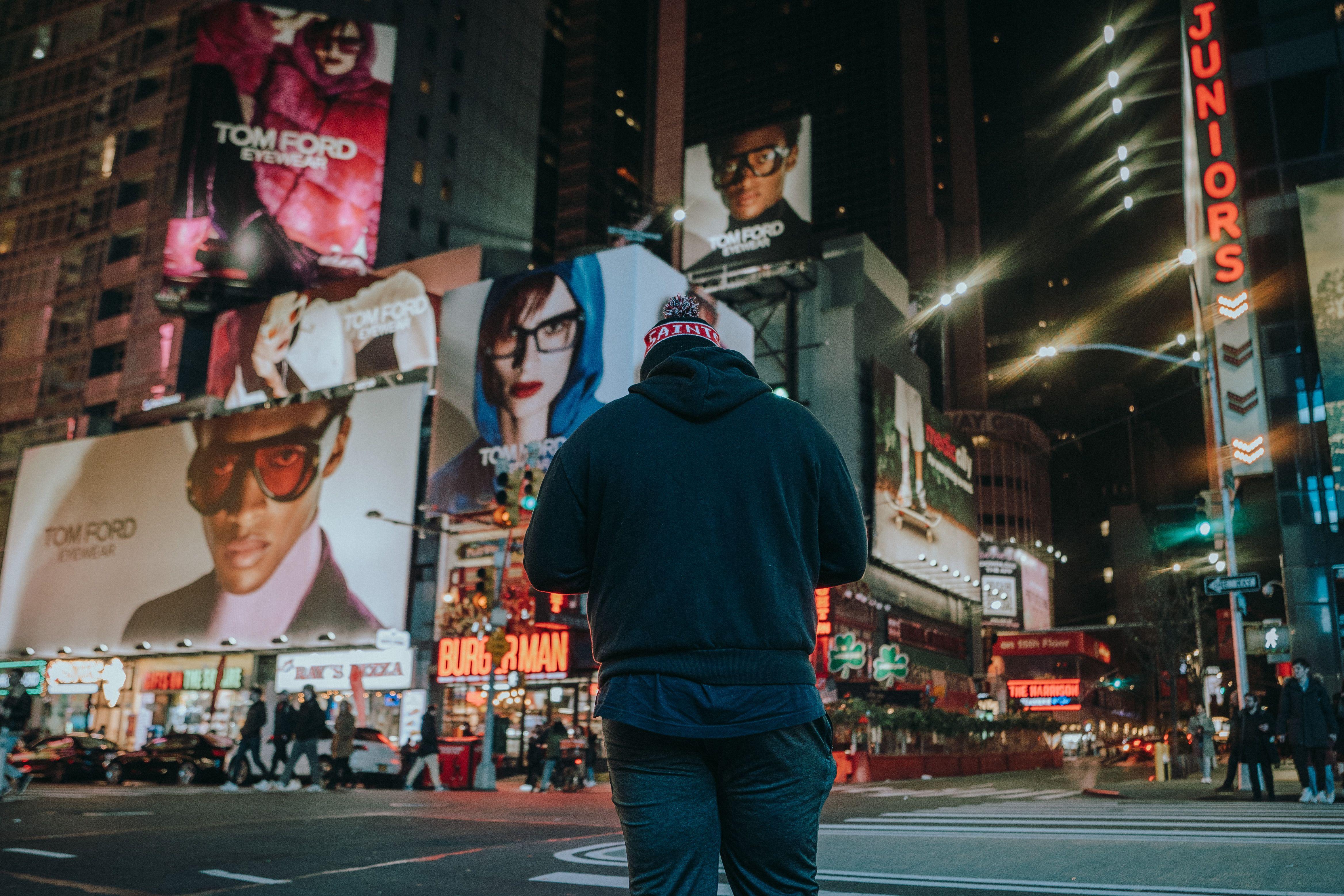 Street scene with a man standing in a vibrant city at night, surrounded by billboards.
