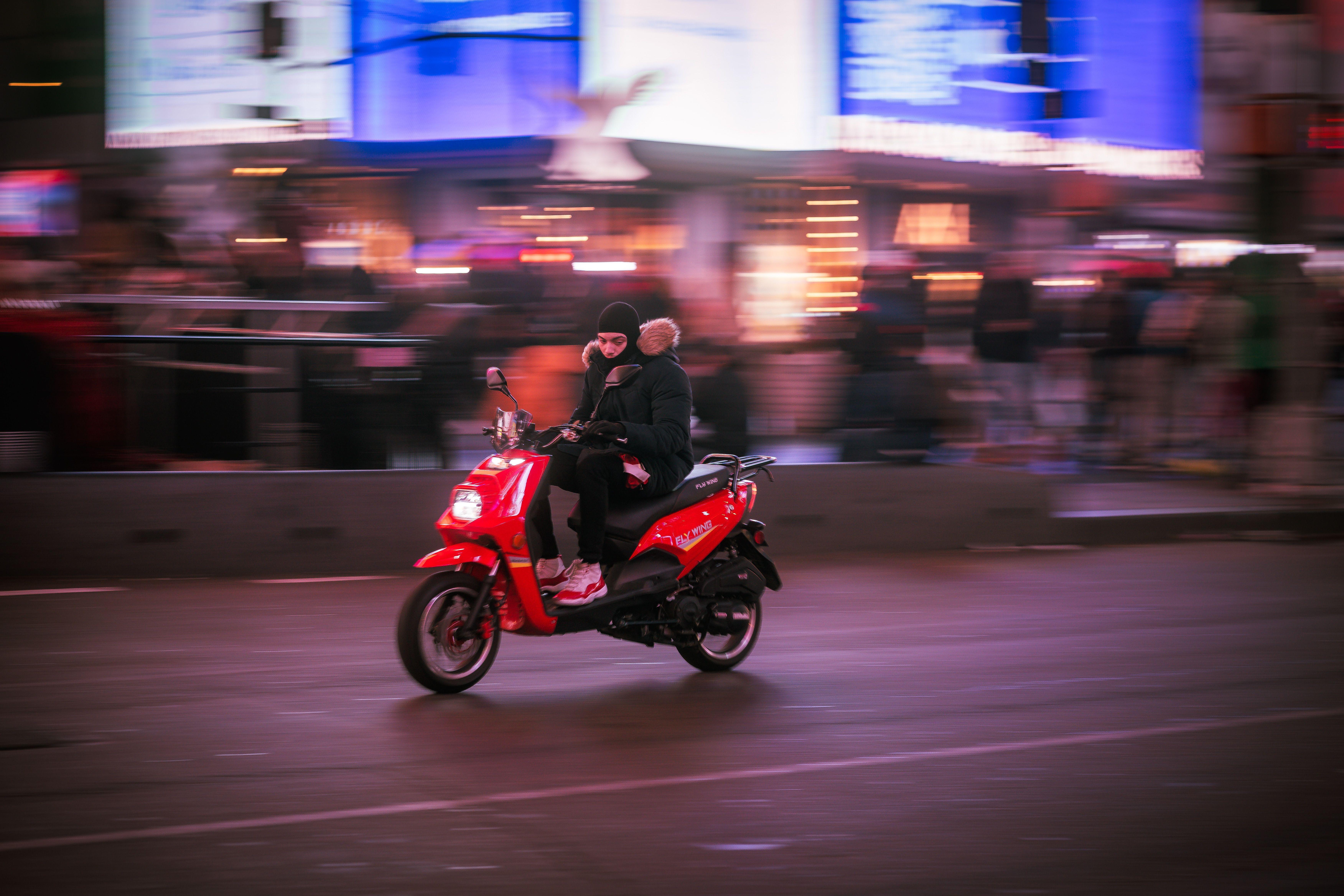 A person rides a red scooter through a vibrant city street at night.