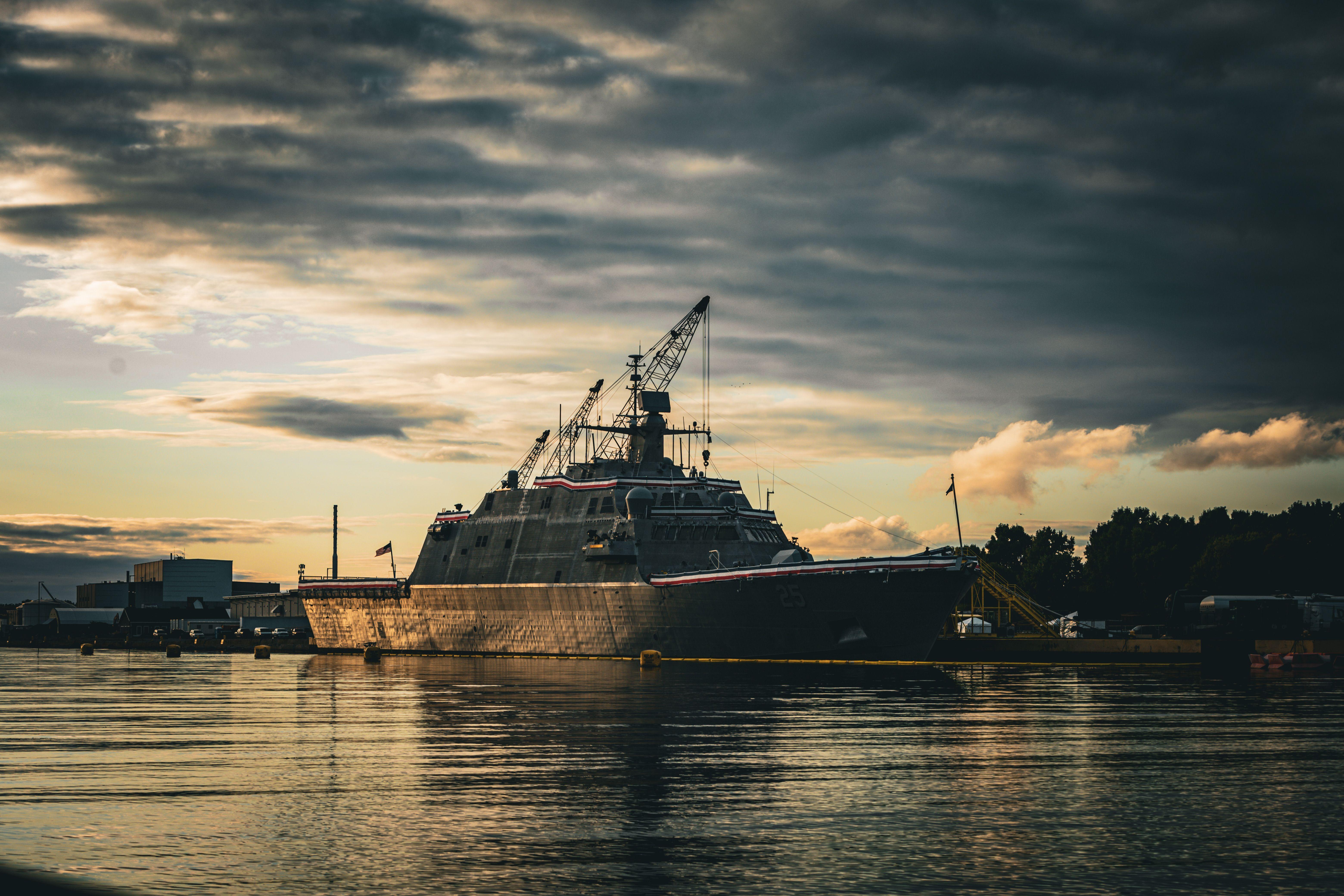 A military vessel docked at Marinette Harbor during a dramatic sunset with overcast clouds.