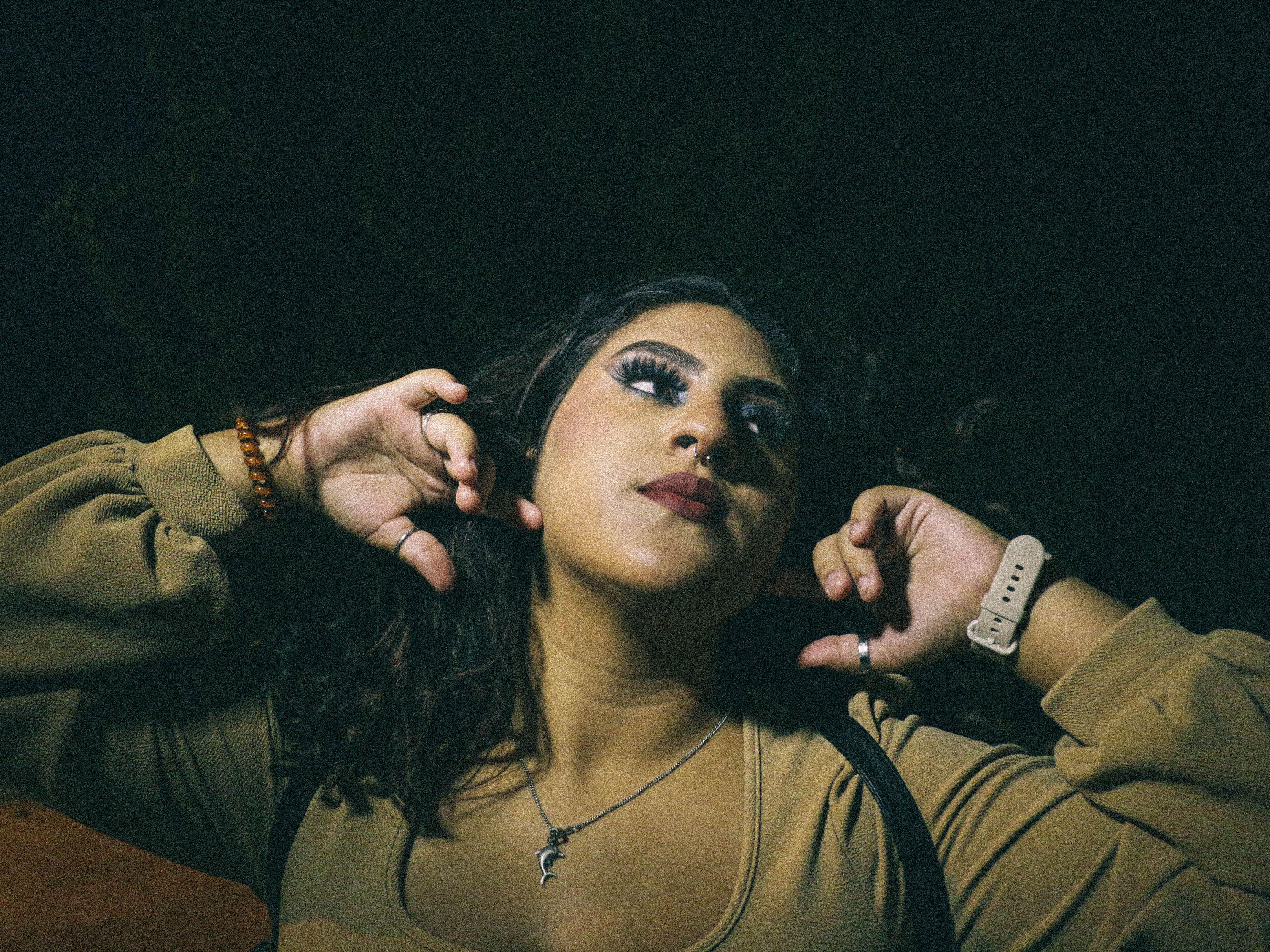 A striking portrait of a woman gazing up with dramatic lighting and raised hands.