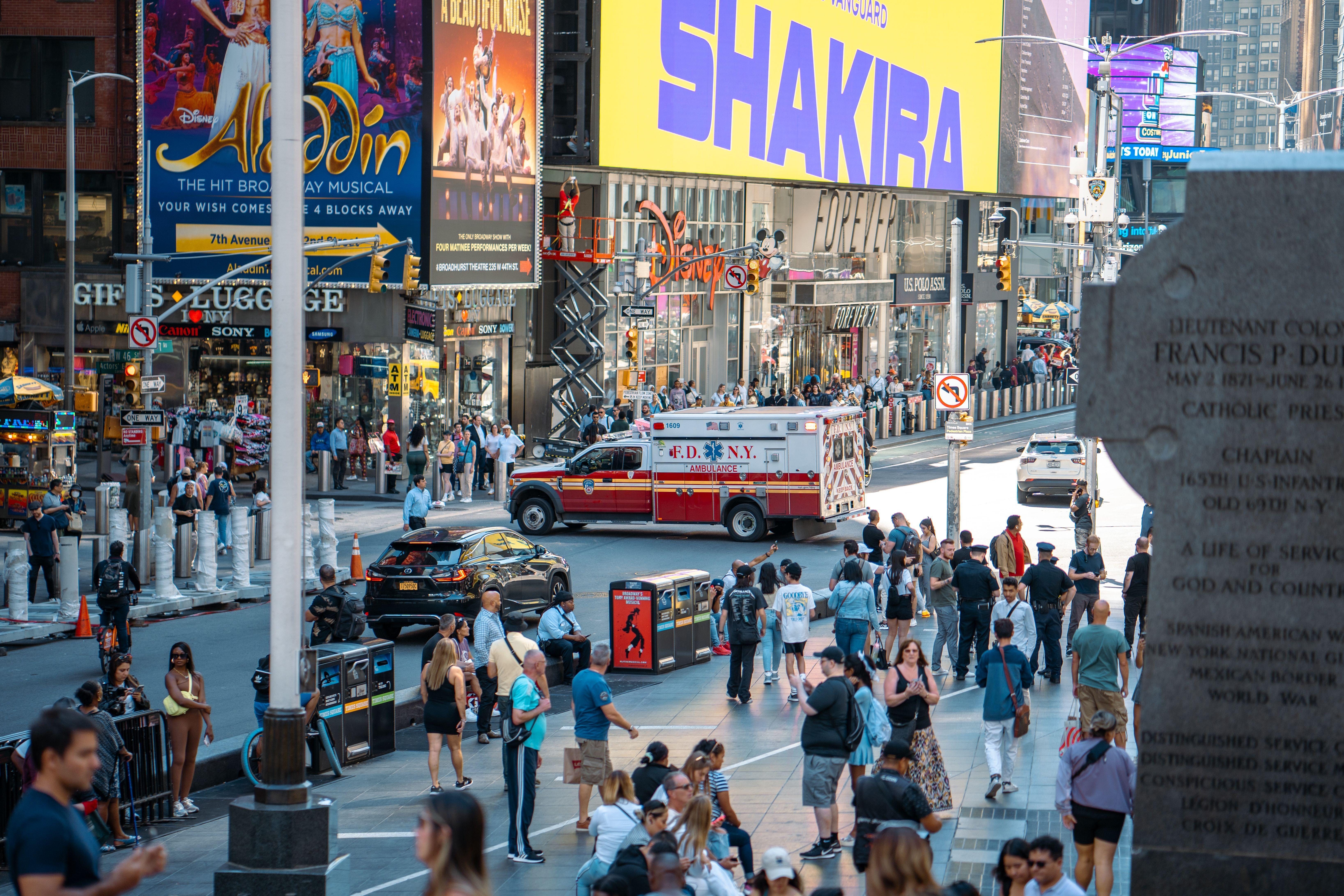 A vibrant view of Times Square, New York City, featuring a busy street with people and an FDNY ambulance.