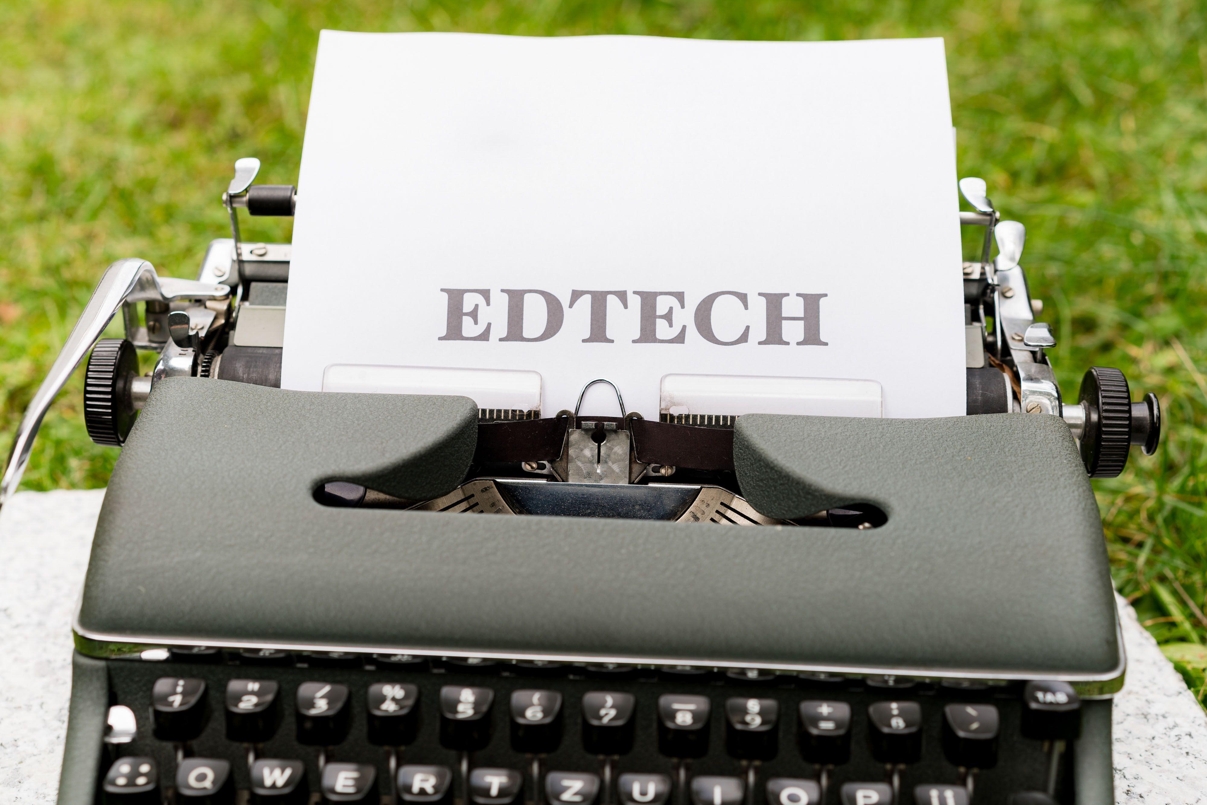 A vintage typewriter displays 'EdTech' on paper, set outdoors on grass.
