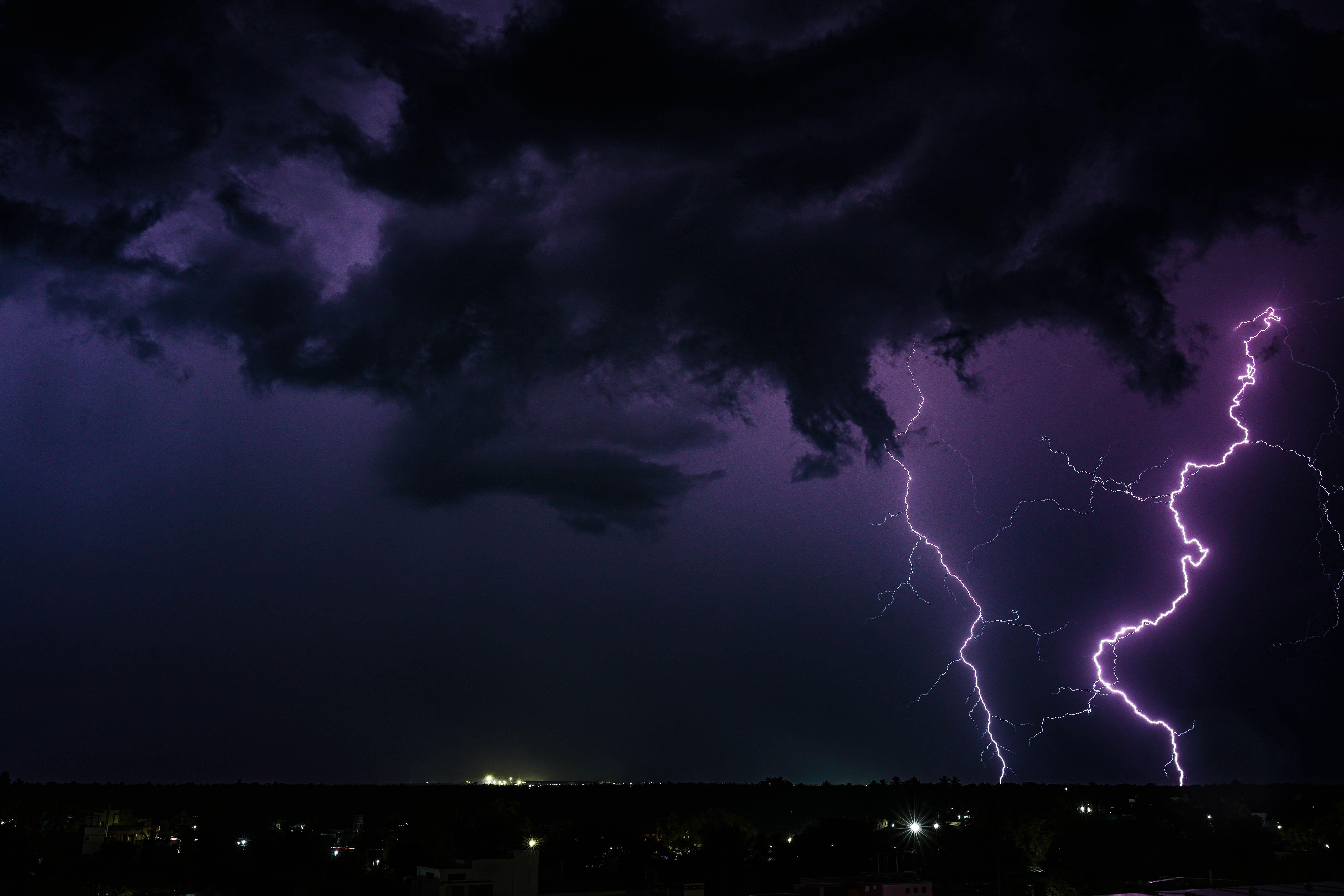 A powerful thunderstorm with dramatic lightning strikes over a city at night in India.