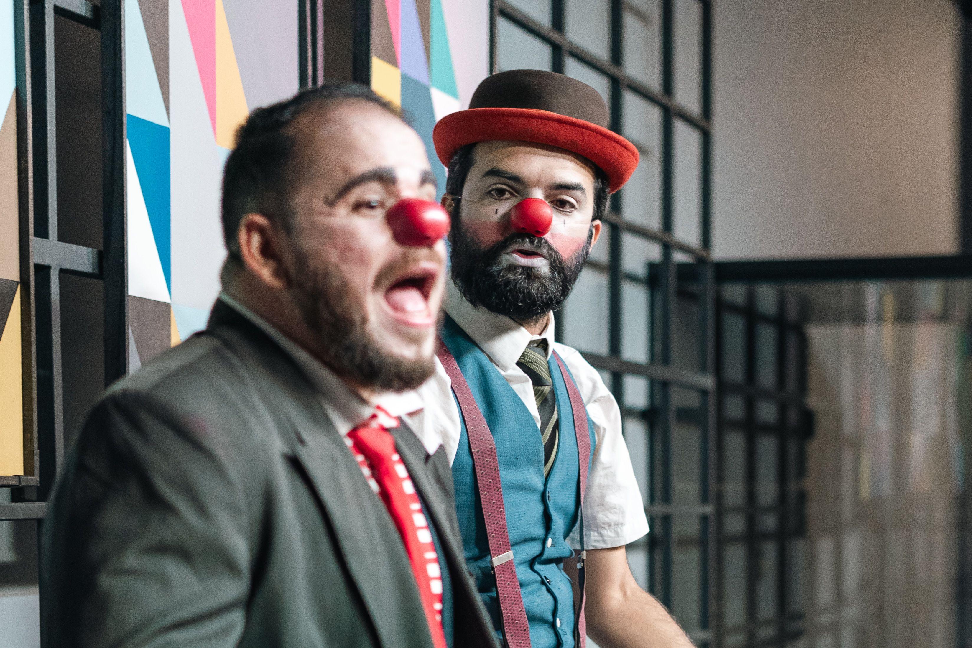 Two male clowns with red noses perform expressively on stage, adding humor and charm.