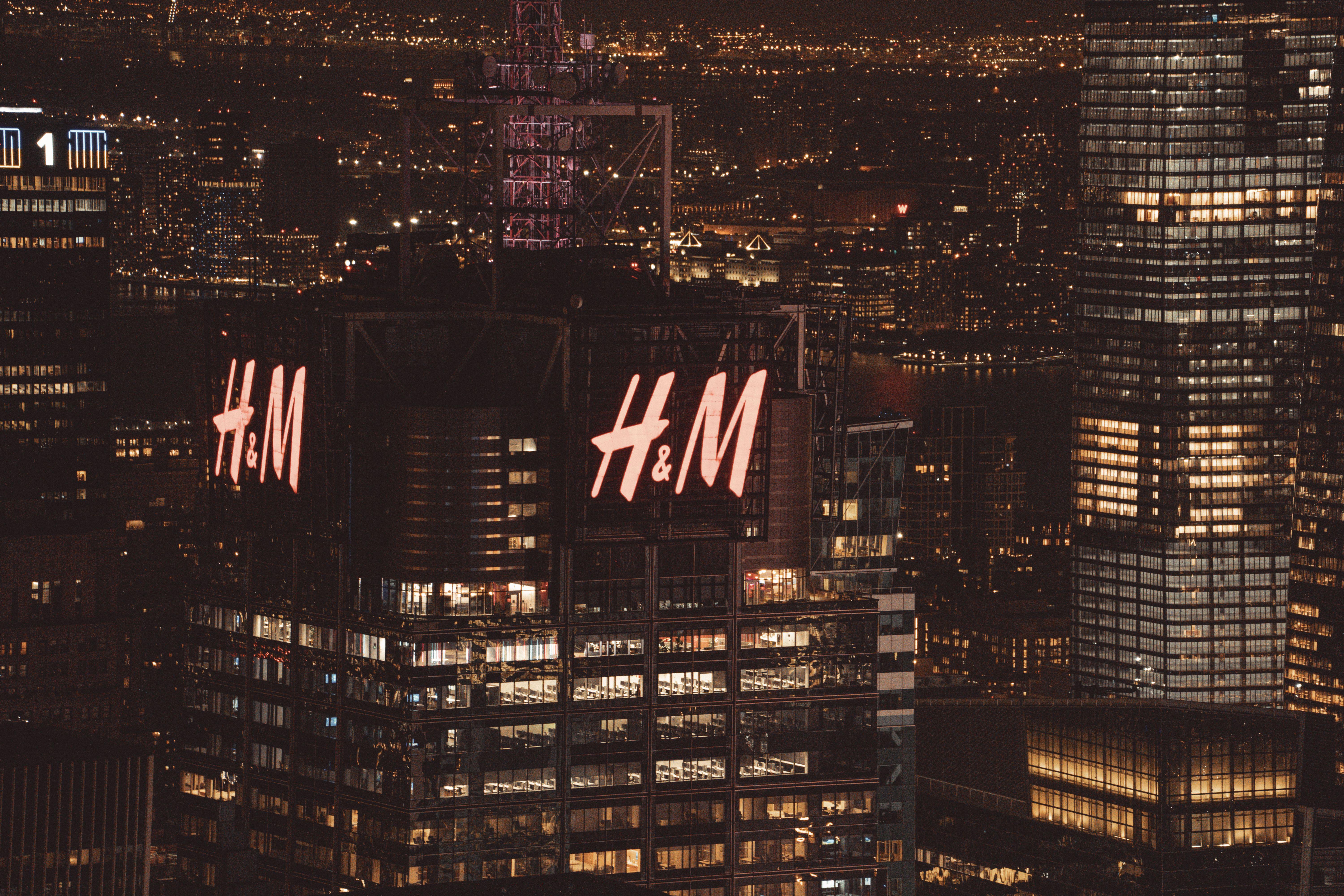 High-angle view of illuminated skyscrapers in New York City at night, featuring H&M building lights.