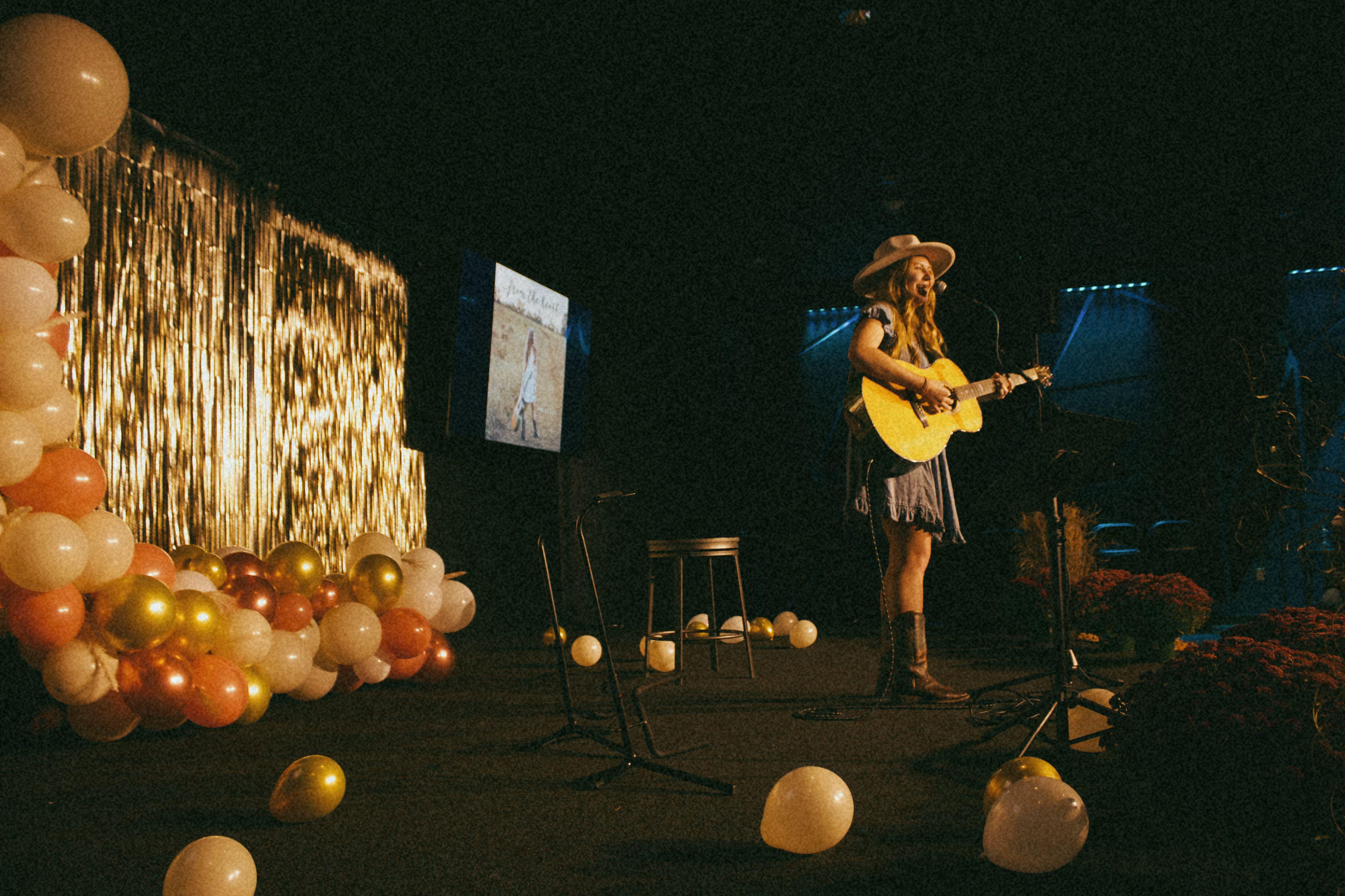 A woman playing guitar on stage decorated with balloons, creating a vibrant performance ambiance.