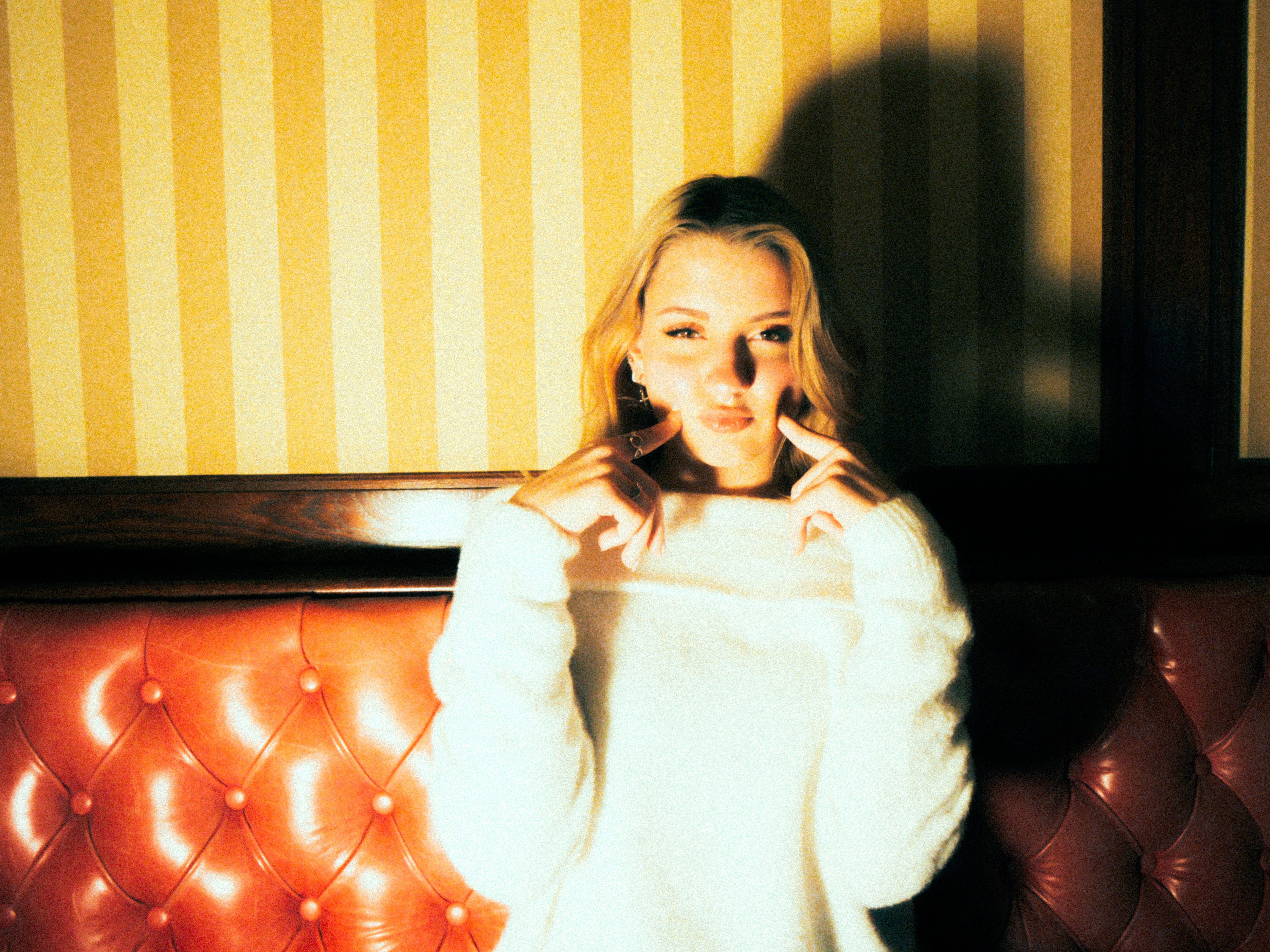 Elegant woman with blonde hair posing indoors with dramatic lighting.