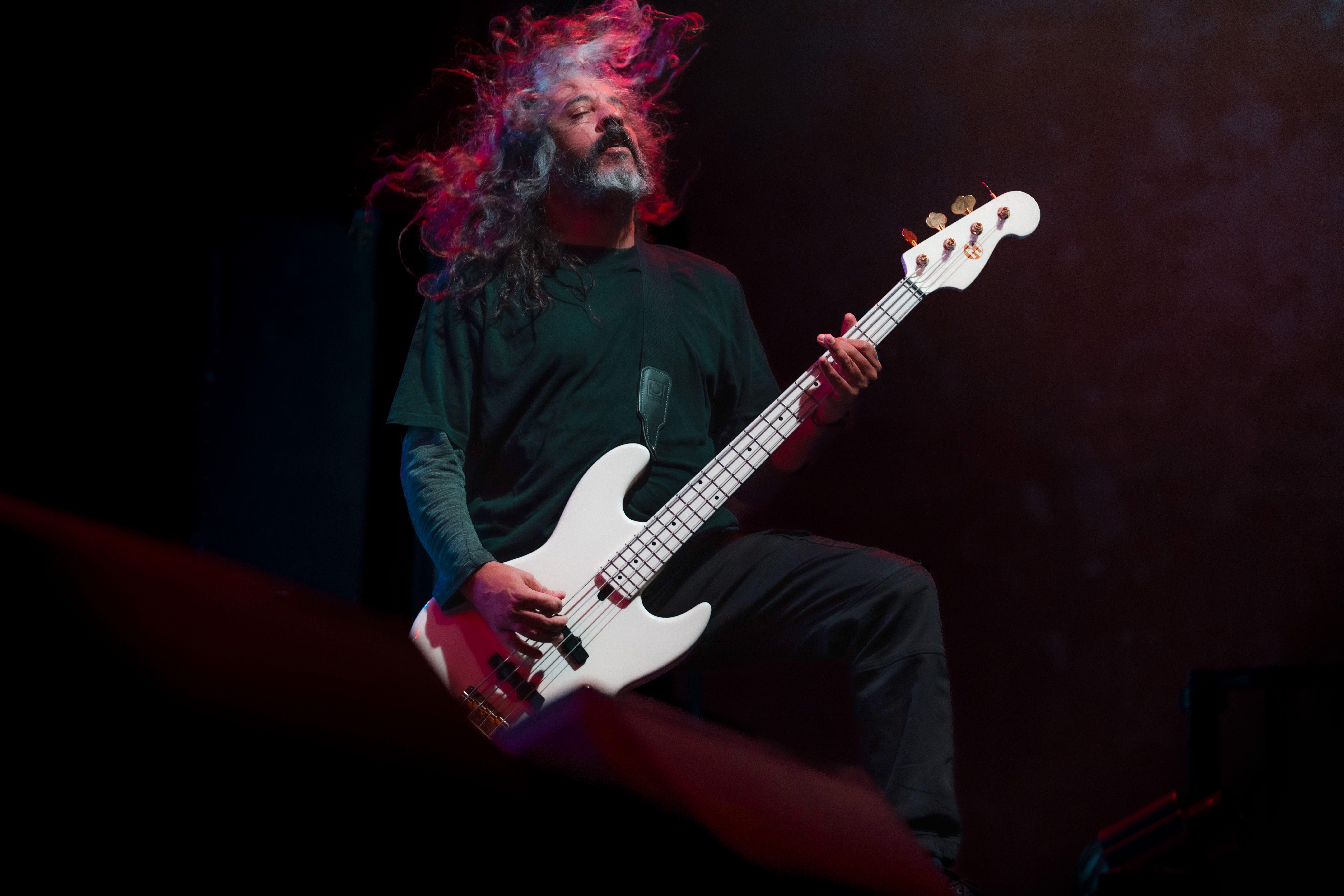 A passionate musician playing bass guitar with long hair flowing on stage.