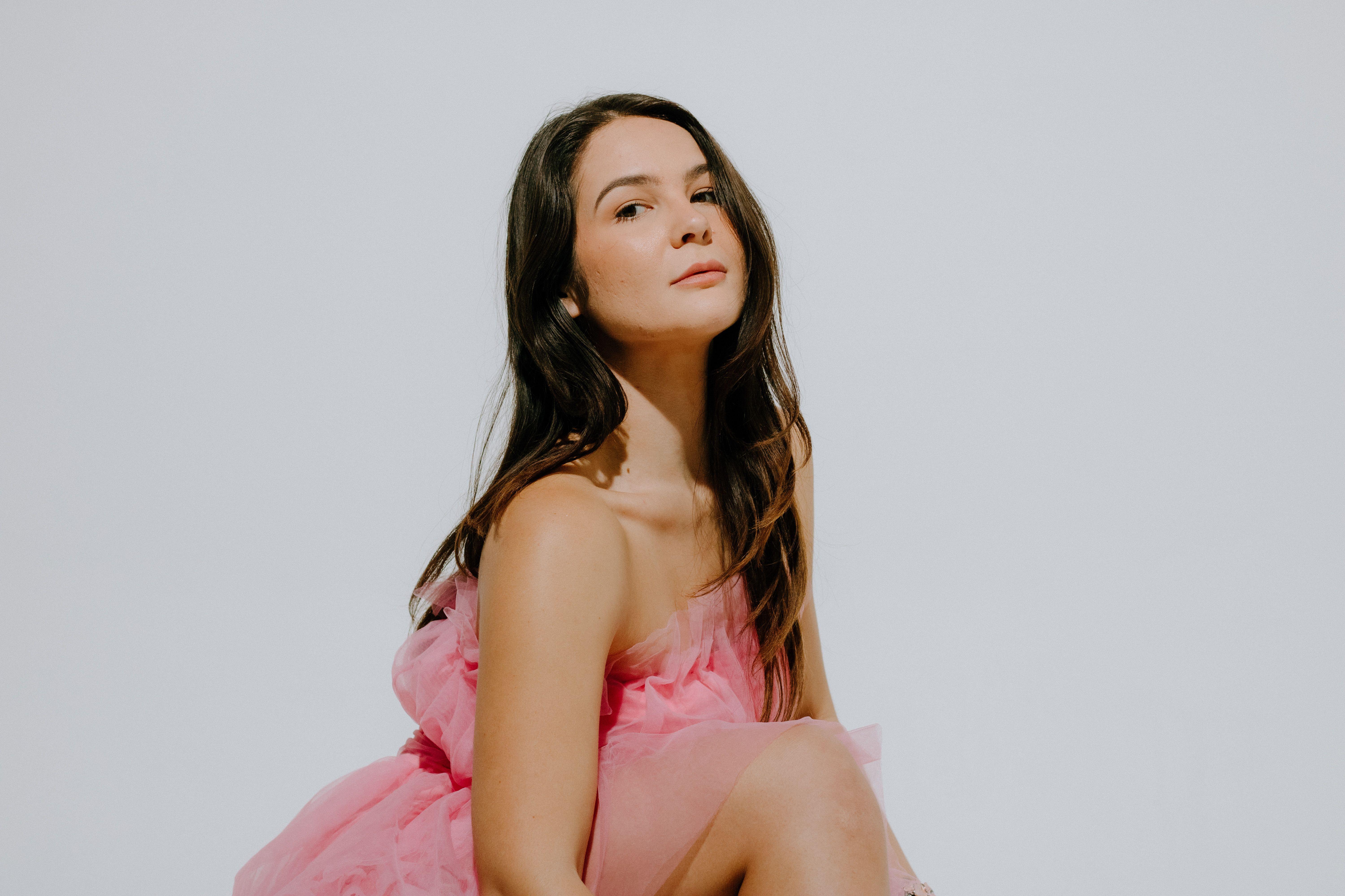 A young woman posing gracefully in a pink dress in a studio setting, exuding elegance and fashion.