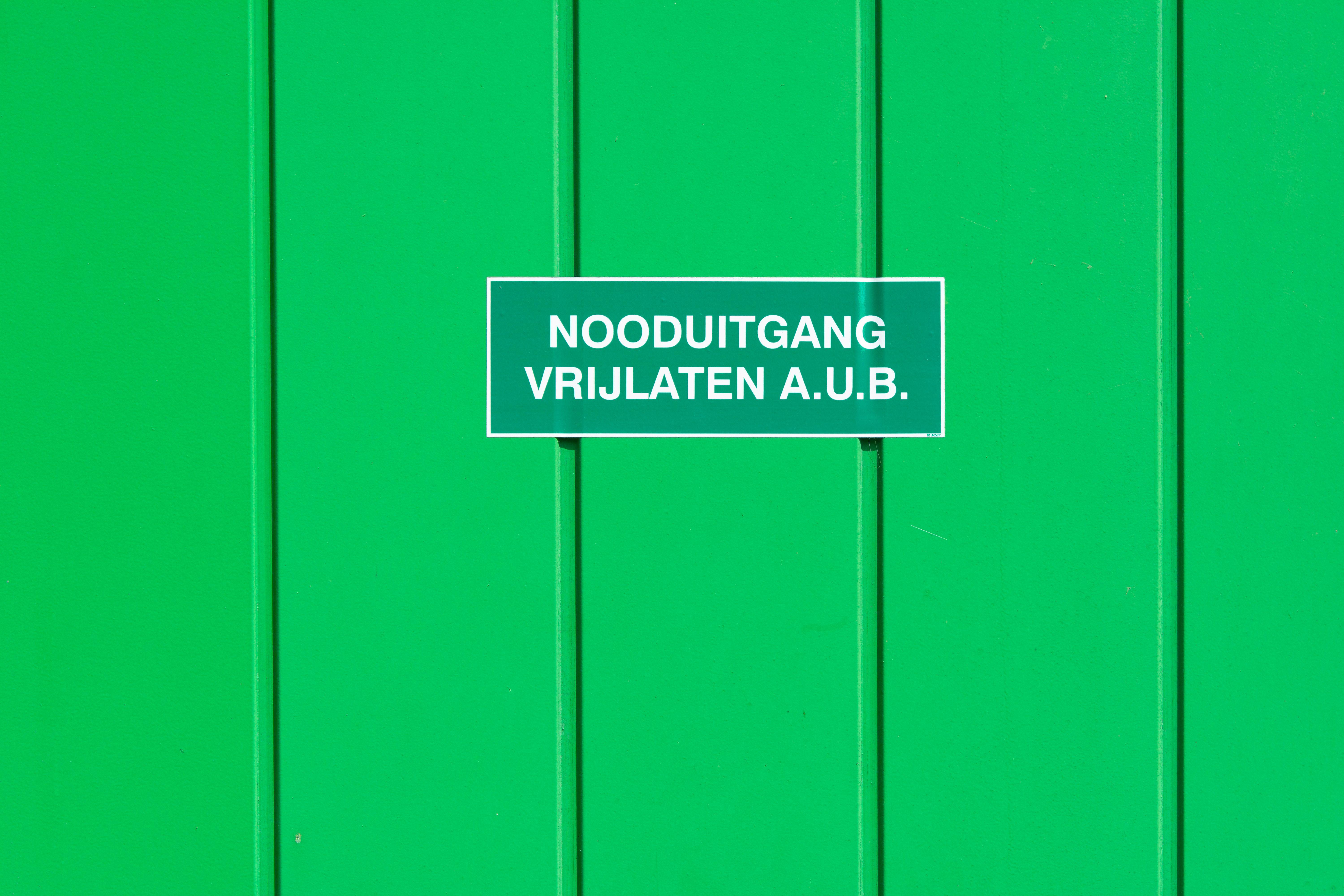 A green metal wall featuring an emergency exit sign in Dutch. Perfect for safety-themed graphics.