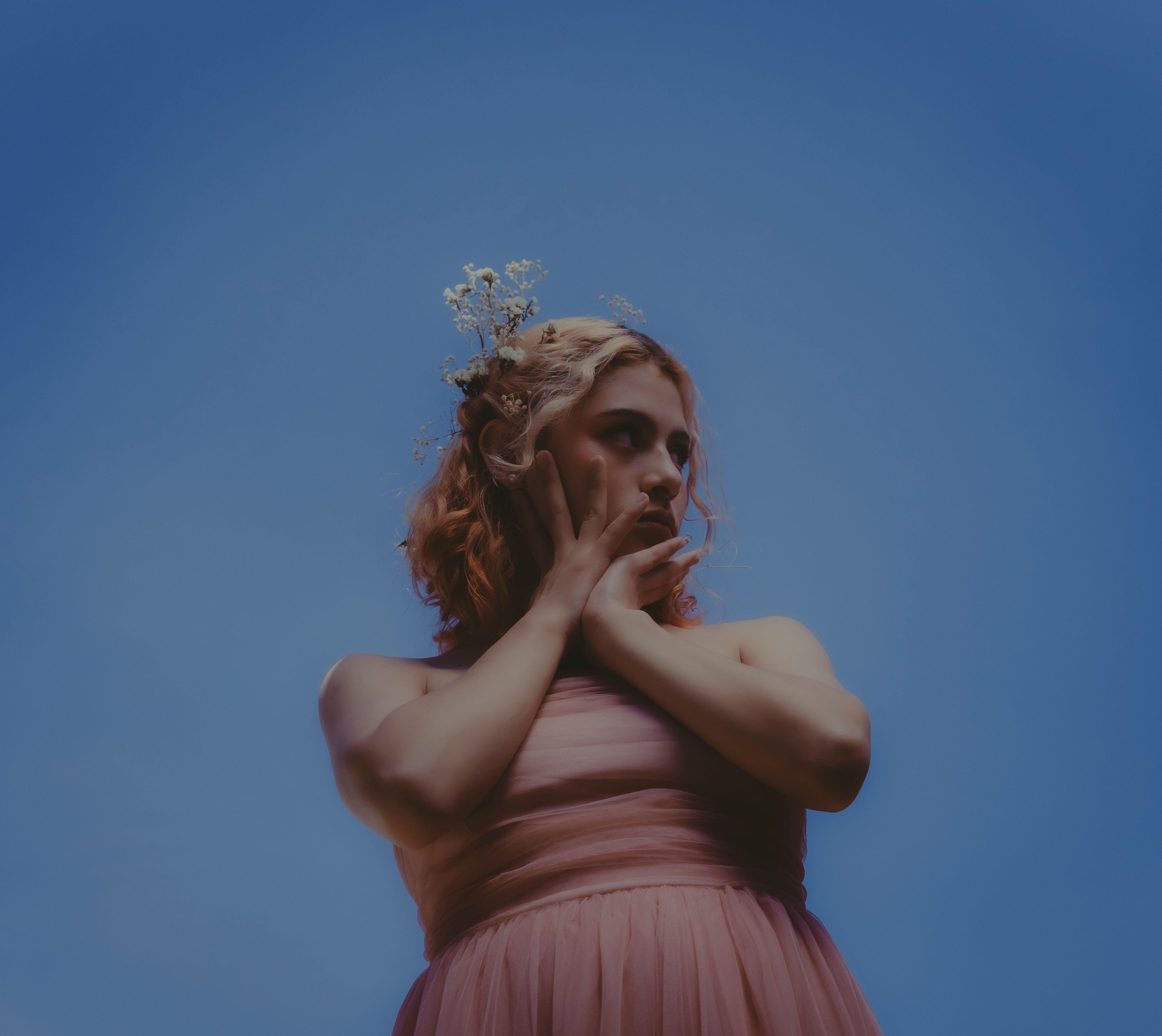 Fashion portrait of a woman in a pink dress against a vibrant clear sky, featuring a floral headpiece.