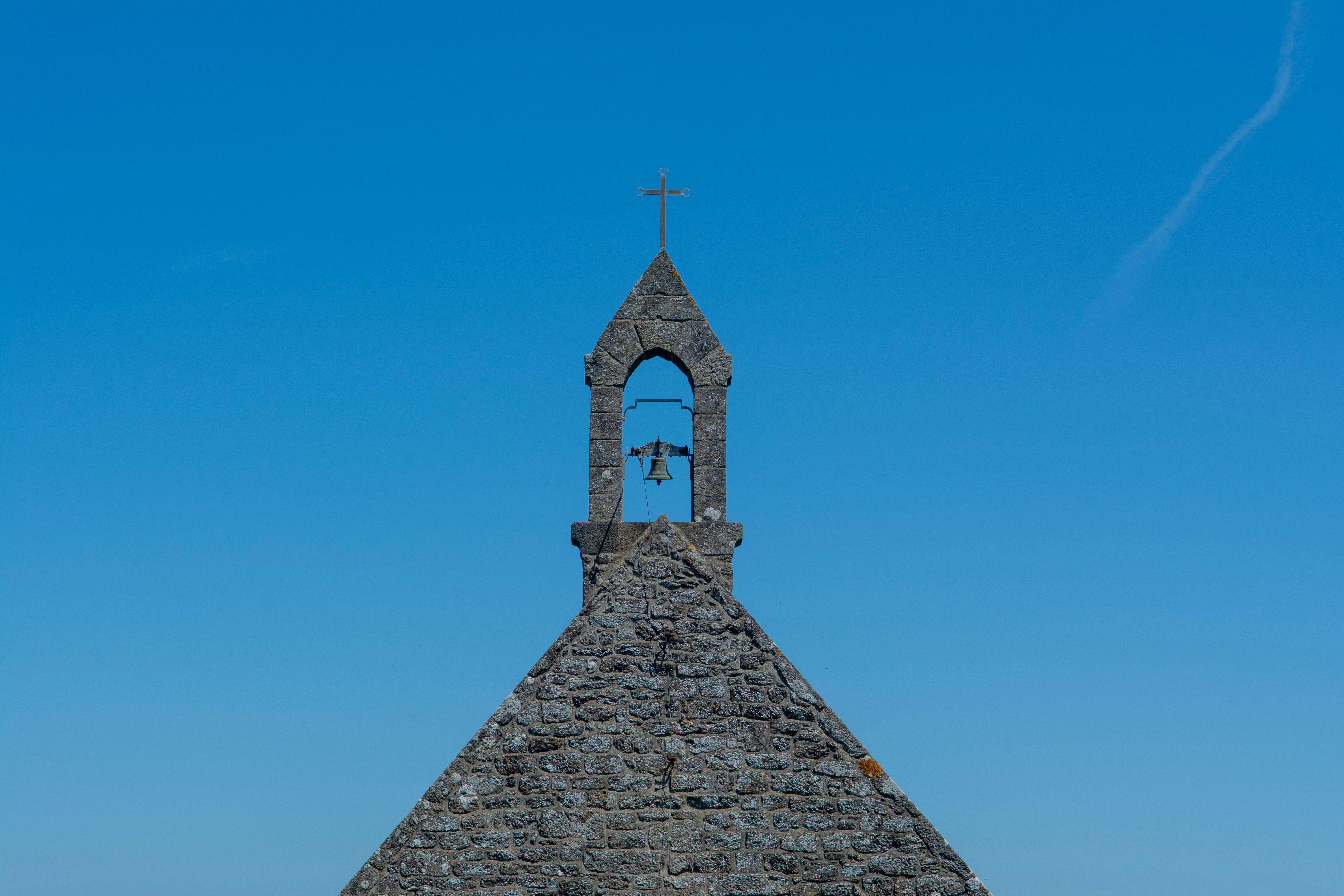 Serene view of a stone chapel bell tower against a clear blue sky, showcasing architecture.