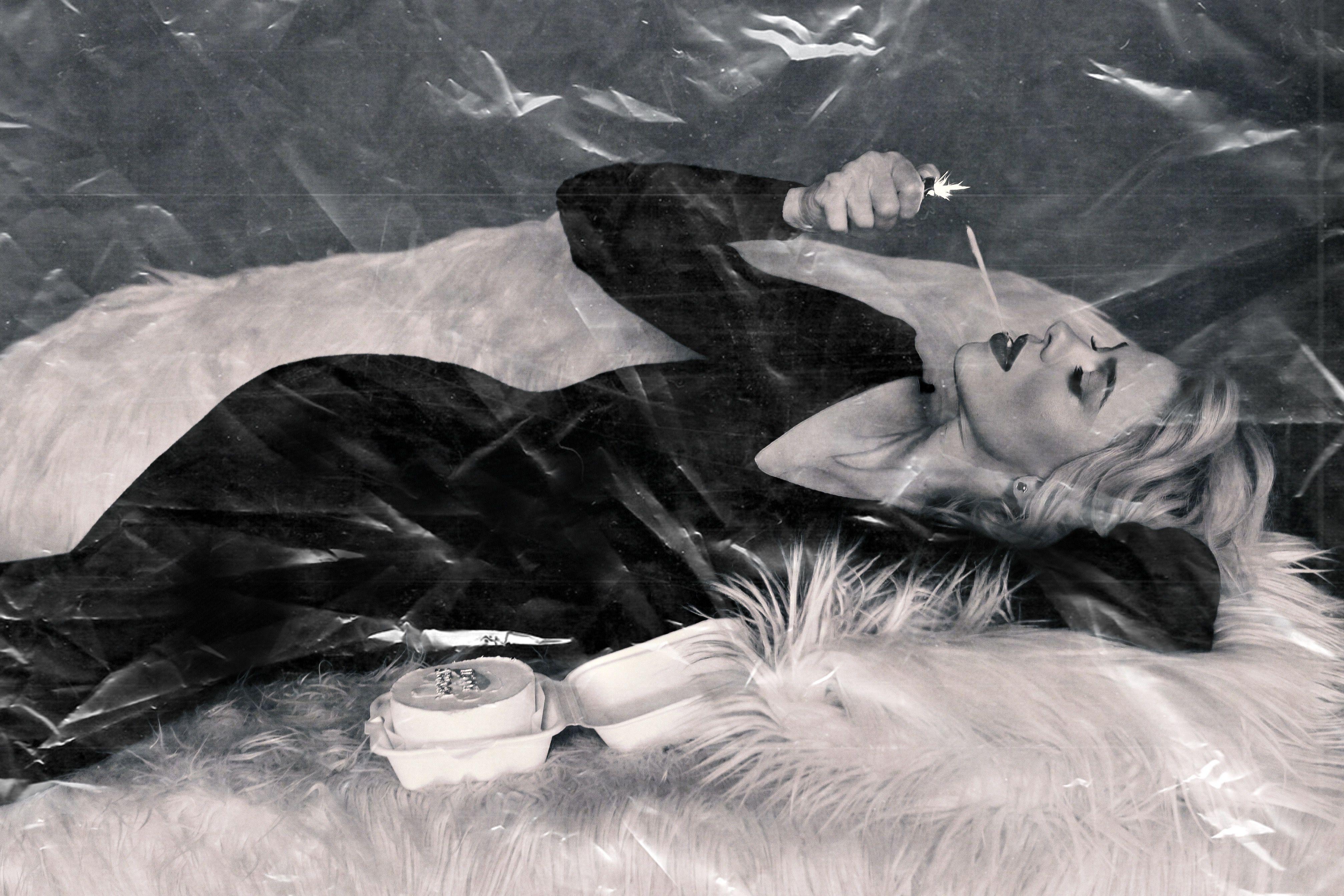 Stylish woman in vintage attire smoking, lying down in a black and white photograph.